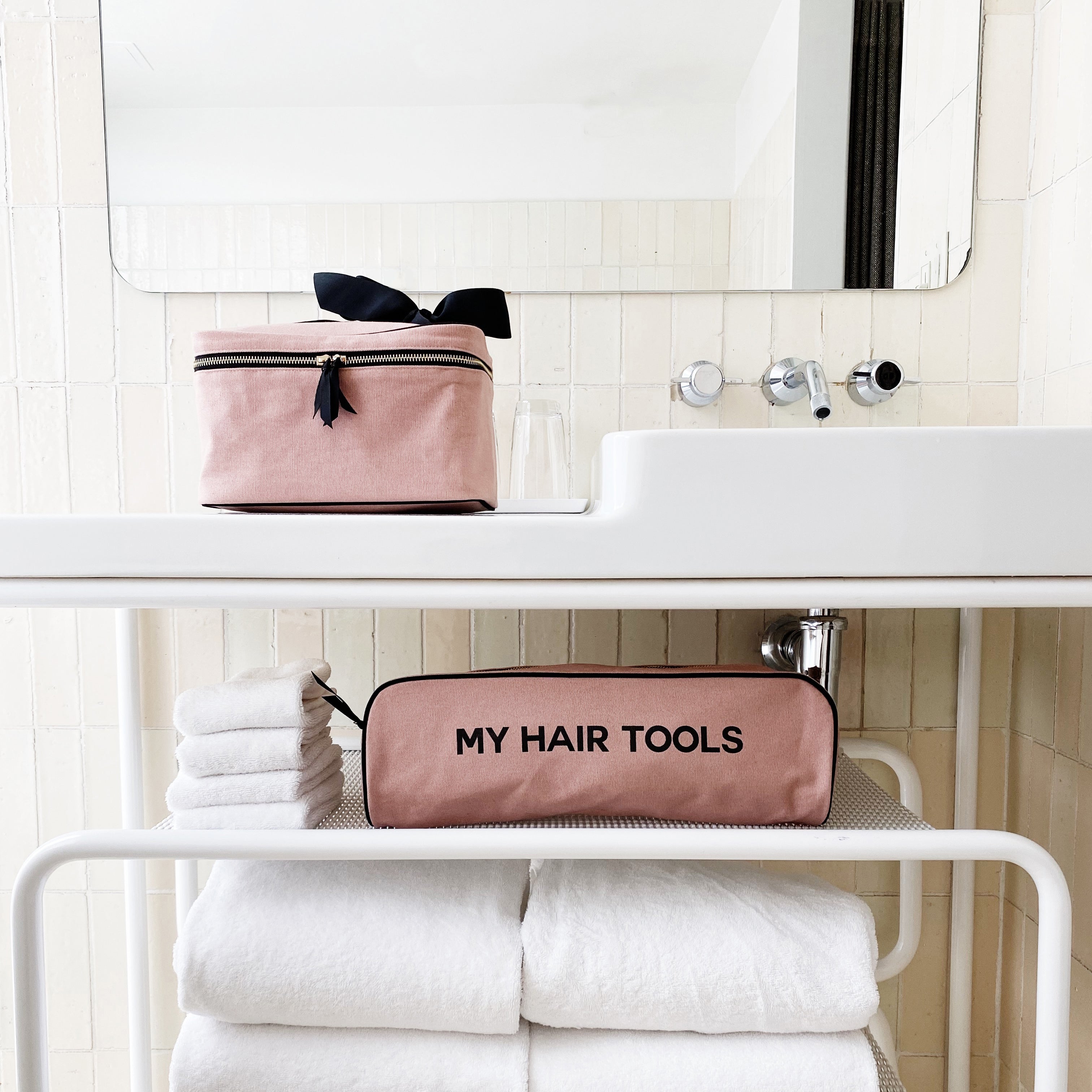 Bag-all Medium Box Makeup & Toiletry in blush pink with black bow, featuring laminated striped interior and 'My Hair Tools' text, displayed on white bathroom counter with matching case below