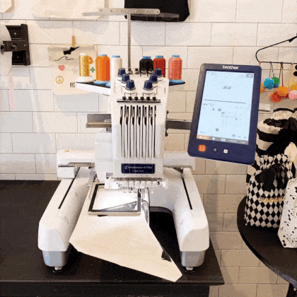 Brother embroidery machine stitching colorful threads on white fabric in a workshop with Bag-all branding nearby
