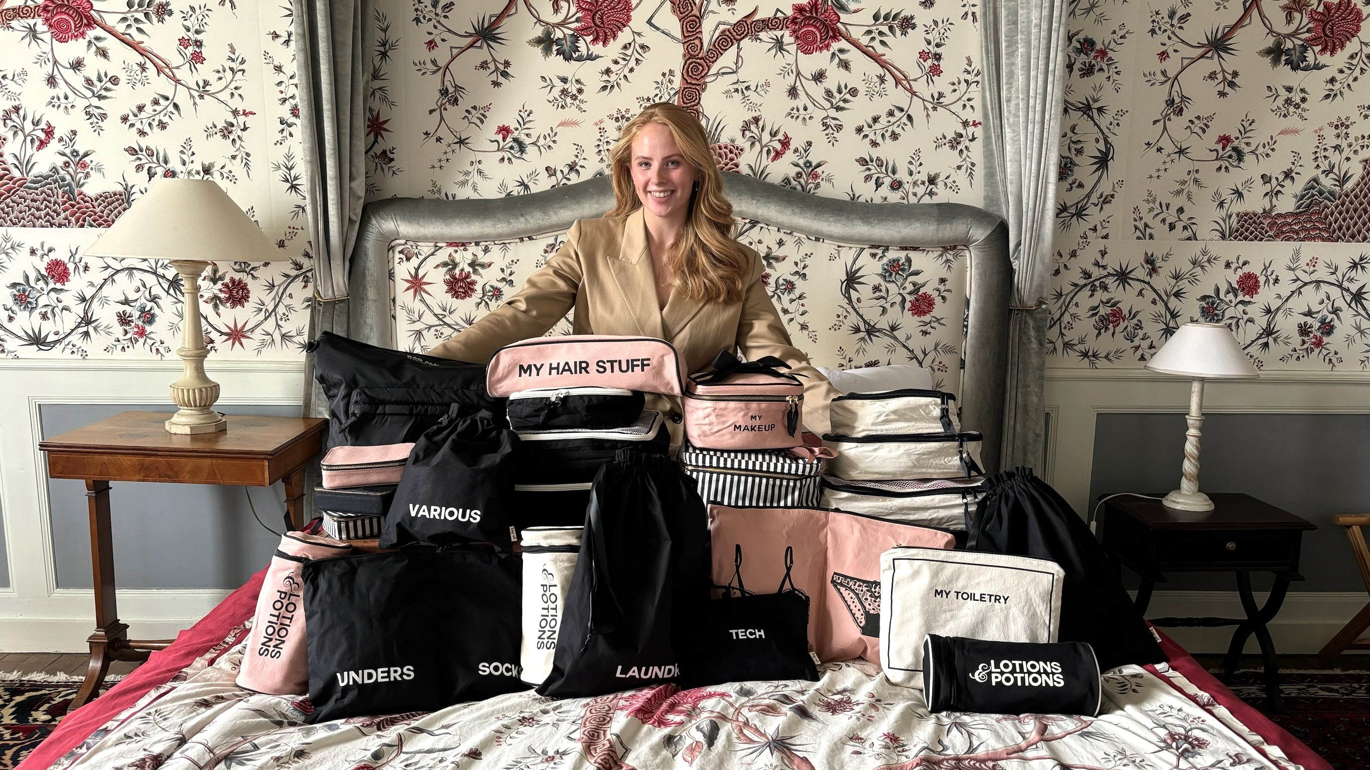 Woman sitting on a bed surrounded by various personalized cotton travel bags and packing cubes labeled for organized packing by Bag-all.