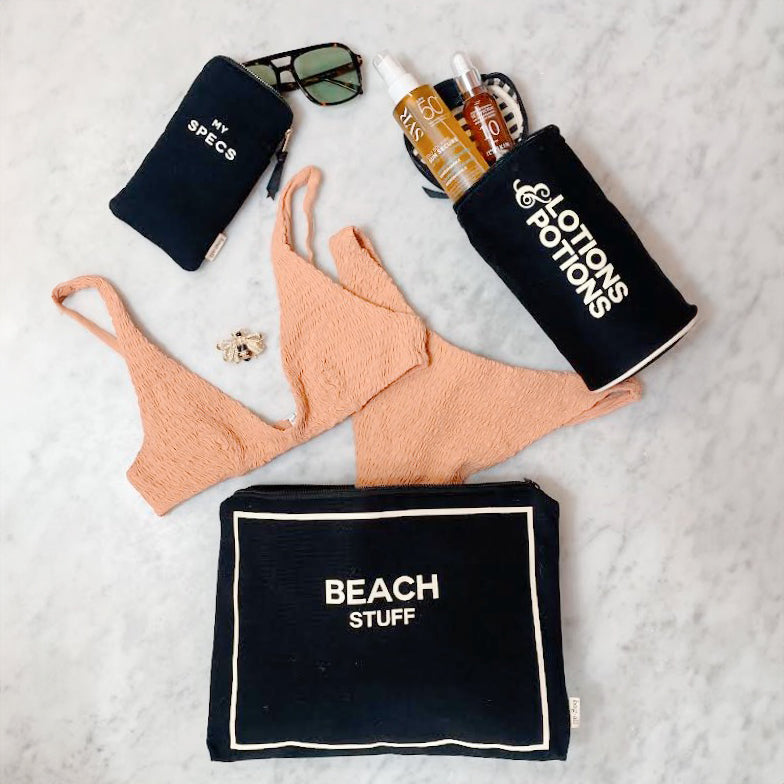 Bag-all Stylish Beach Essential Set featuring black organizer bags for sunglasses, lotions, and beach items with white text, displayed with coral bikini and beach accessories on marble surface