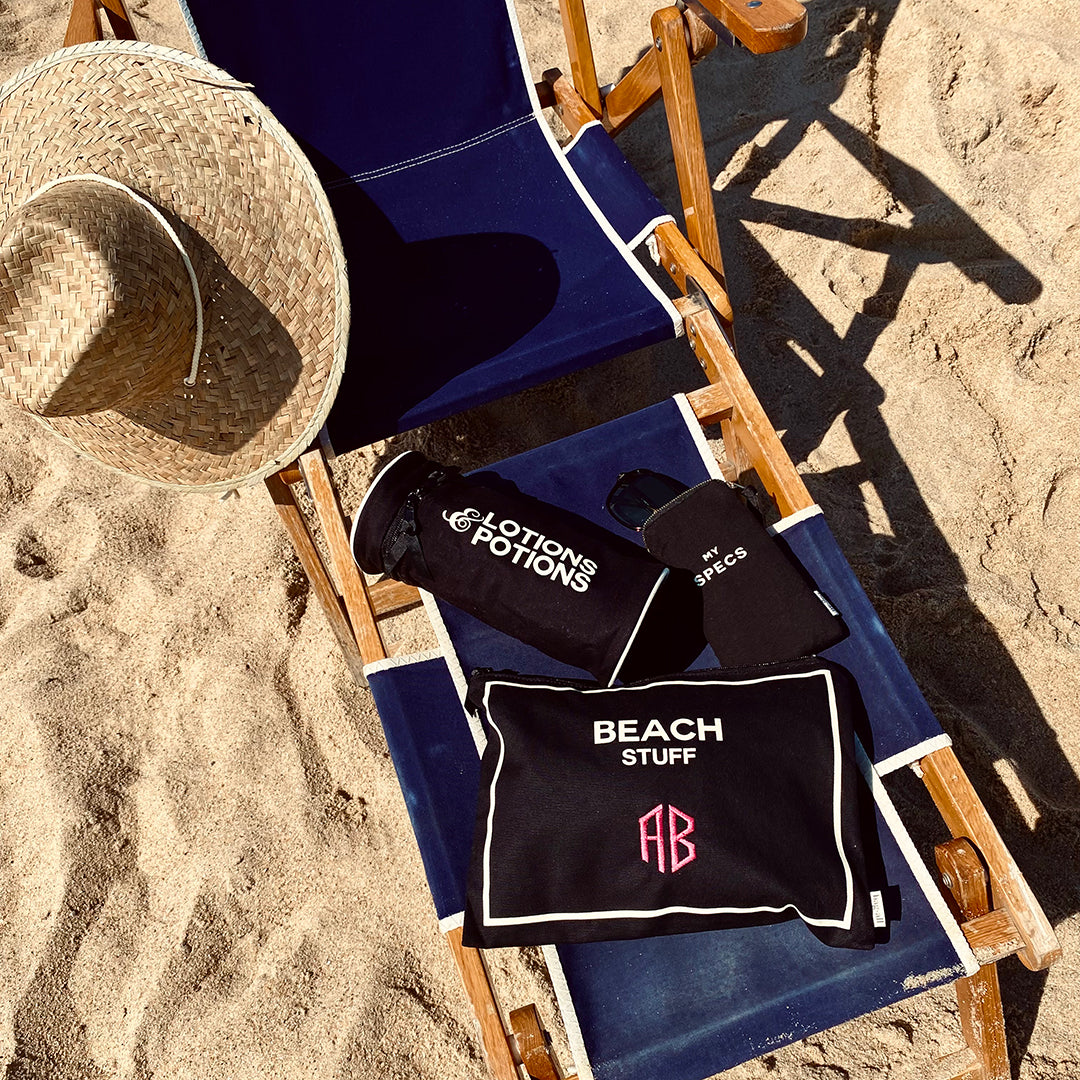 Bag-all Stylish Beach Essential Set in black featuring waterproof pouches on beach chair with straw hat, perfect for organizing beach accessories and personal items. Monogrammable cotton bags for seaside organization.