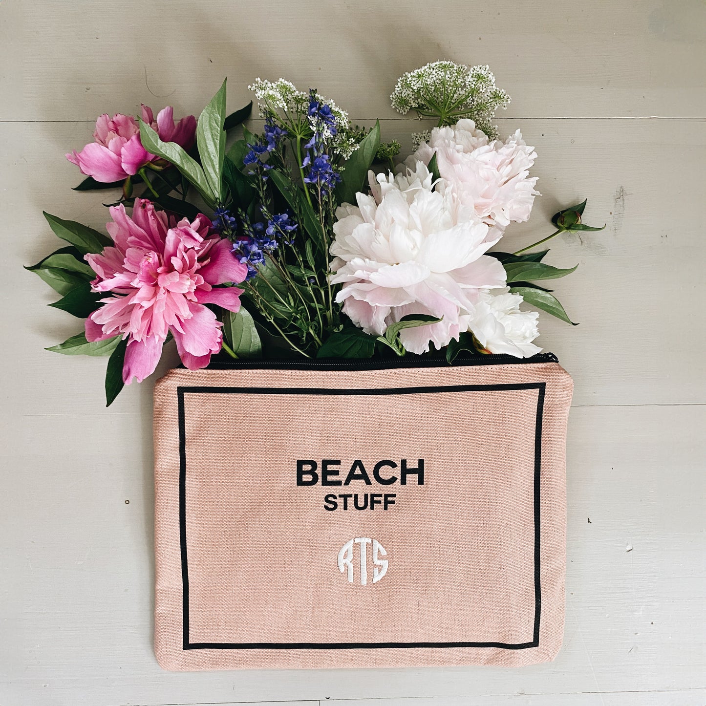 Bag-all pink monogram beach pouch with 'Beach Stuff' text and personalized initials, showcasing waterproof cotton material and black border, styled with pink and white peonies