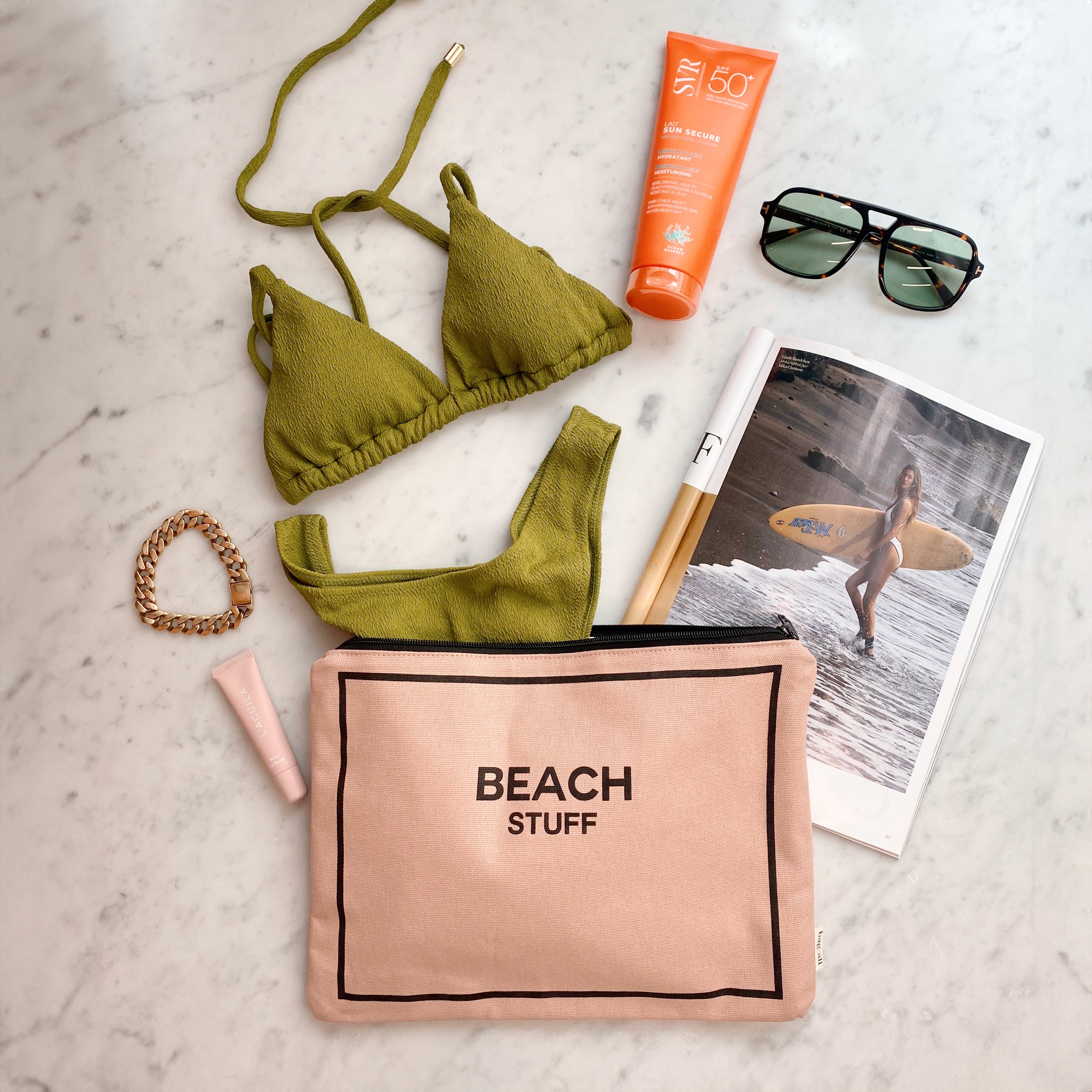 Bag-all Pink Monogram Beach Pouch shown with olive green bikini, sunscreen, sunglasses and beach photo, perfect for organizing beach essentials in waterproof style