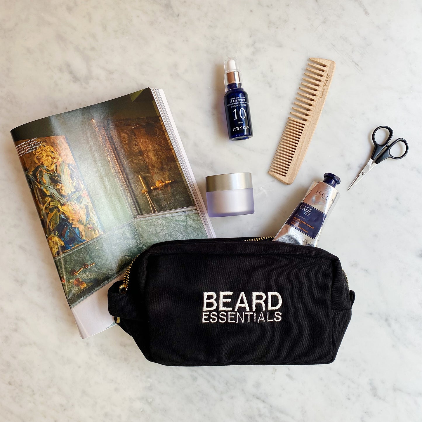 Bag-all Beard Essentials Toiletry Case with grooming tools including wooden comb, scissors, beard oil and cream displayed on marble surface