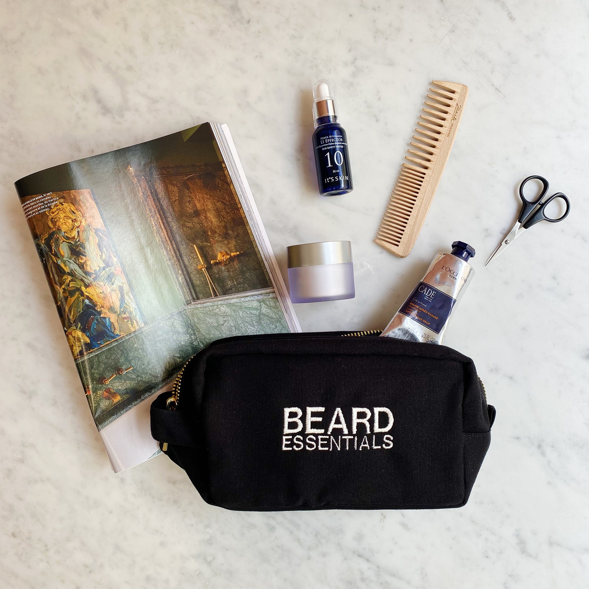 Bag-all Beard Essentials Toiletry Case with grooming tools including wooden comb, scissors, beard oil and cream displayed on marble surface