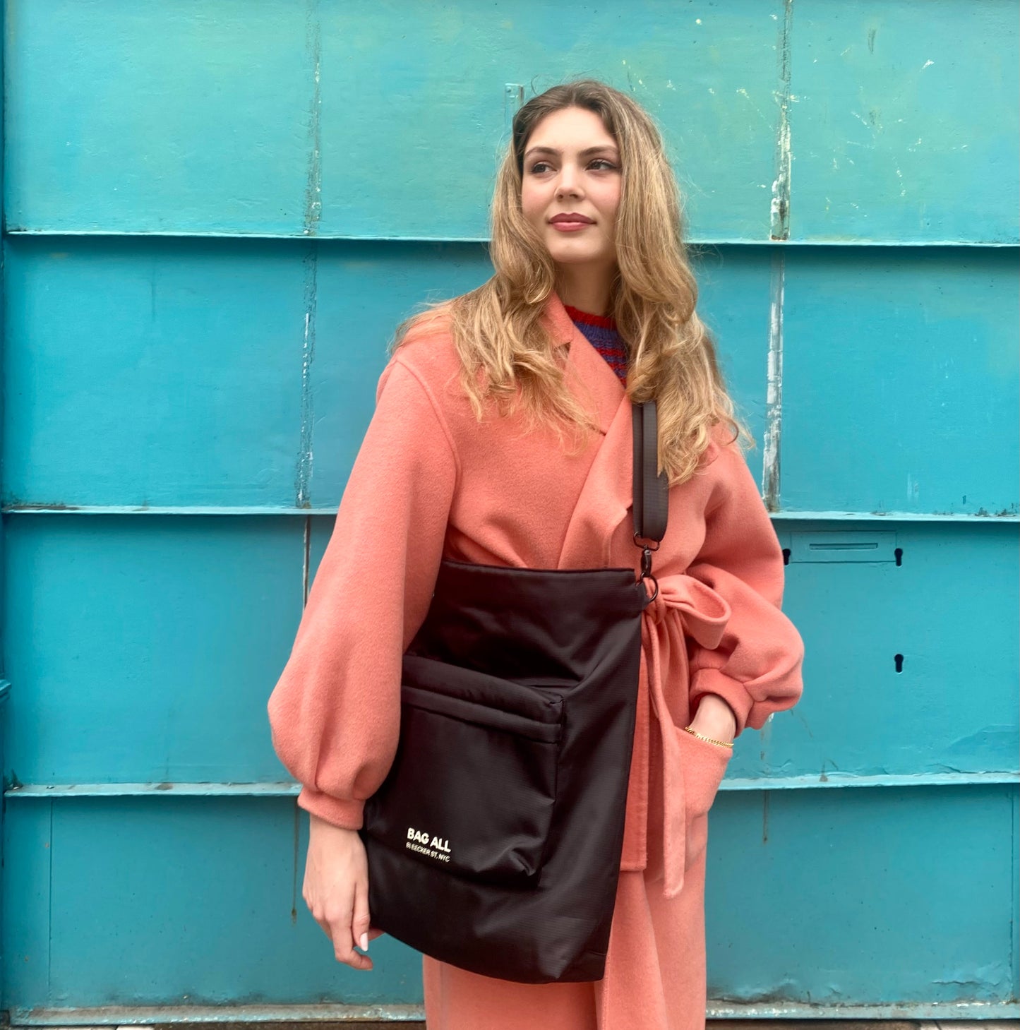 Bag-all City Backpack/Tote in black recycled nylon shown against turquoise wall, demonstrating versatile convertible design with padded laptop protection
