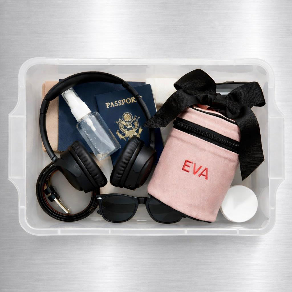 Pink Bag-all Carry On Liquids Case with black ribbon, travel-sized bottles, headphones, passport, sunglasses in clear organizer box
