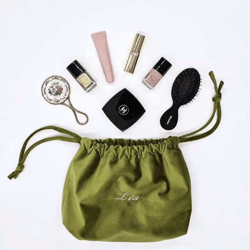 Bag-all green eco velvet drawstring makeup bag personalized with name surrounded by beauty essentials on white background