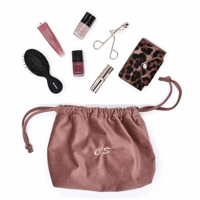 Pink velvet drawstring makeup bag by Bag-all with beauty essentials, brush, and travel accessories neatly arranged nearby