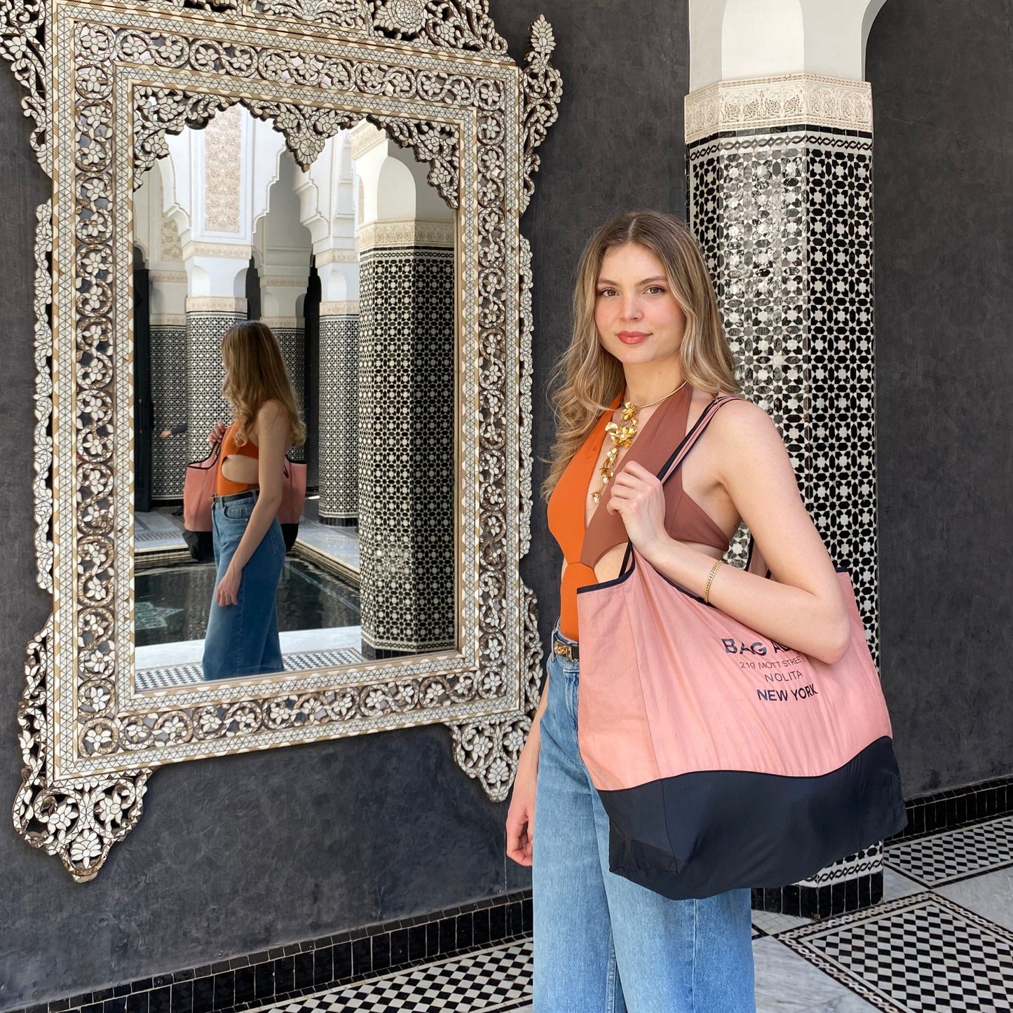 Bag-all Folding Shopping Bag with Zipper Pocket Pouch shown in stylish pink and black, featuring compact foldable design and secure storage compartment, modeled in ornate Moroccan-style interior with decorative mirror and geometric tiles