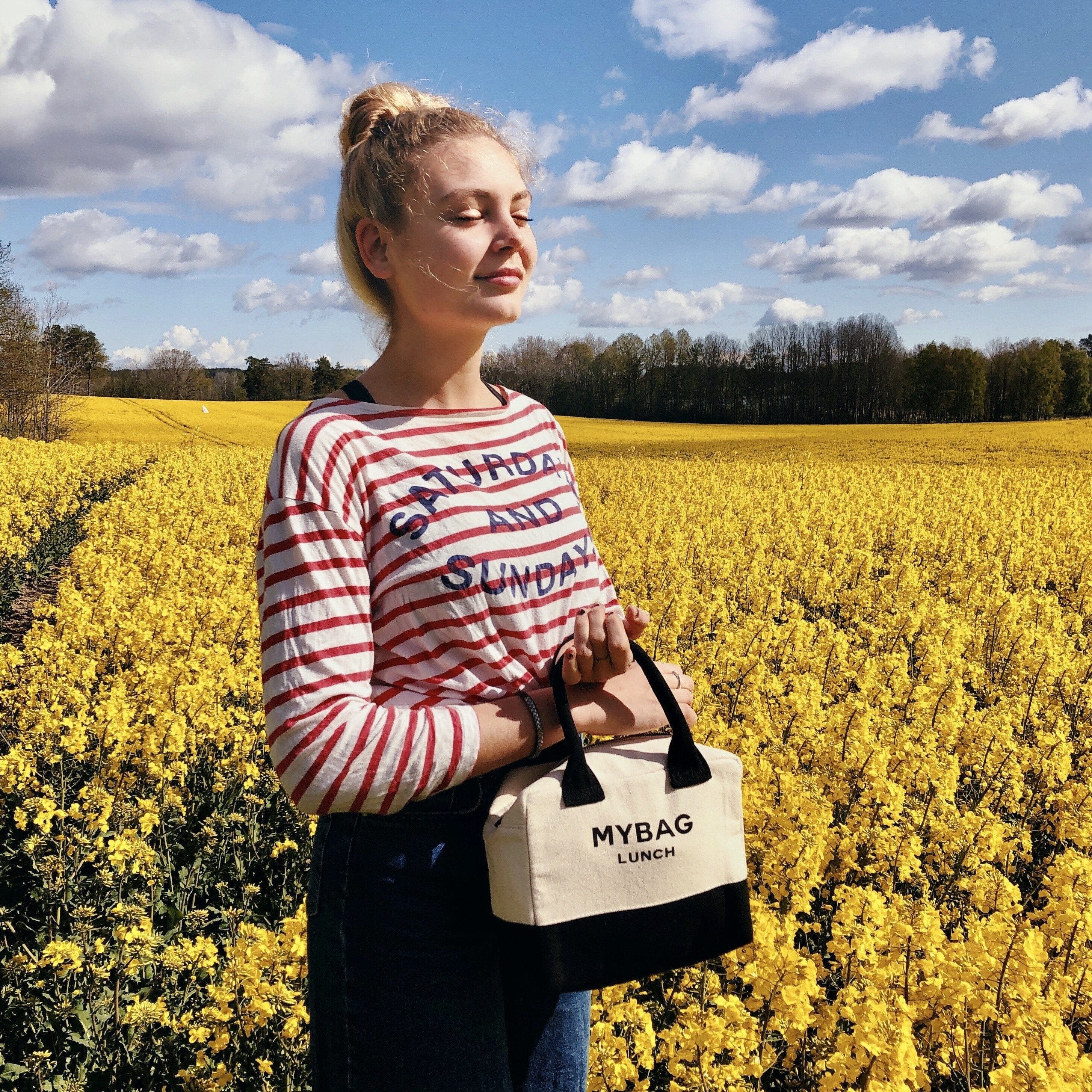 Bag-all Insulated Lunch Box in cream with black accents shown in vibrant yellow rapeseed field, featuring durable cotton fabric and practical carrying handle