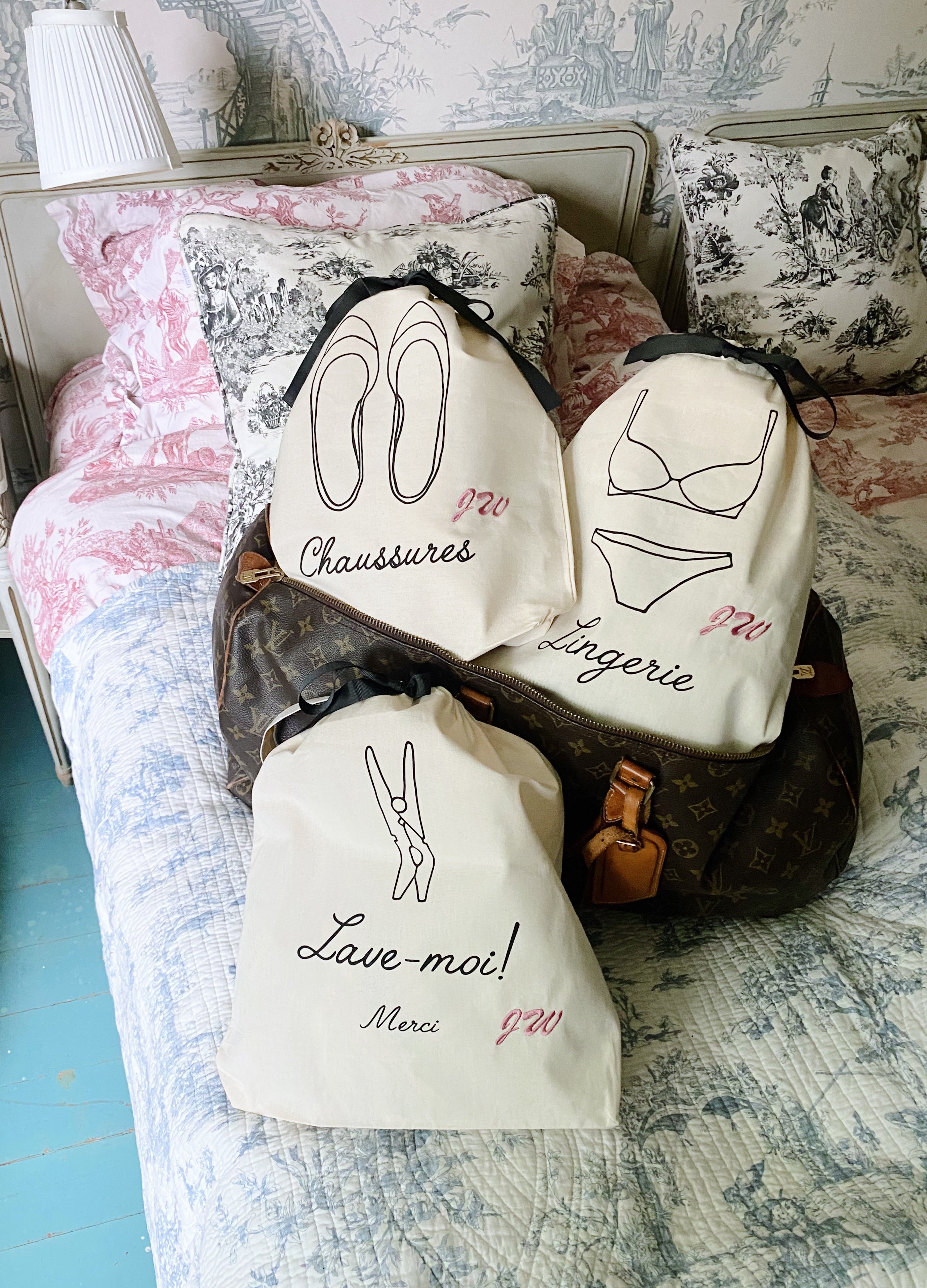 Bag-all French Collection Travel 3-pack cream cotton organizing bags with French text and illustrations for shoes, lingerie, and laundry, displayed on toile-patterned bedding