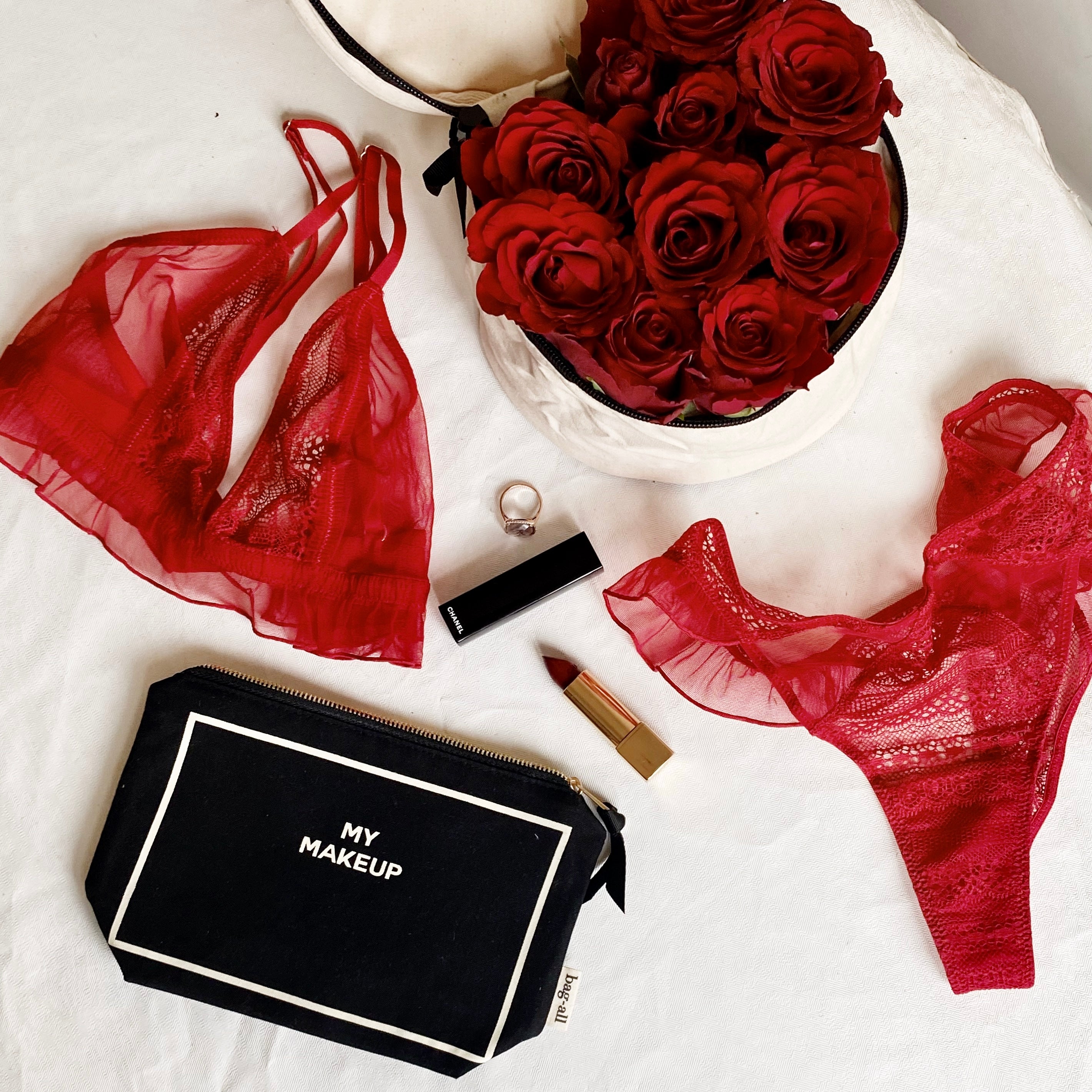 Black Bag-all makeup organizer pouch with red lingerie, lipstick, ring, and bouquet of red roses on white background