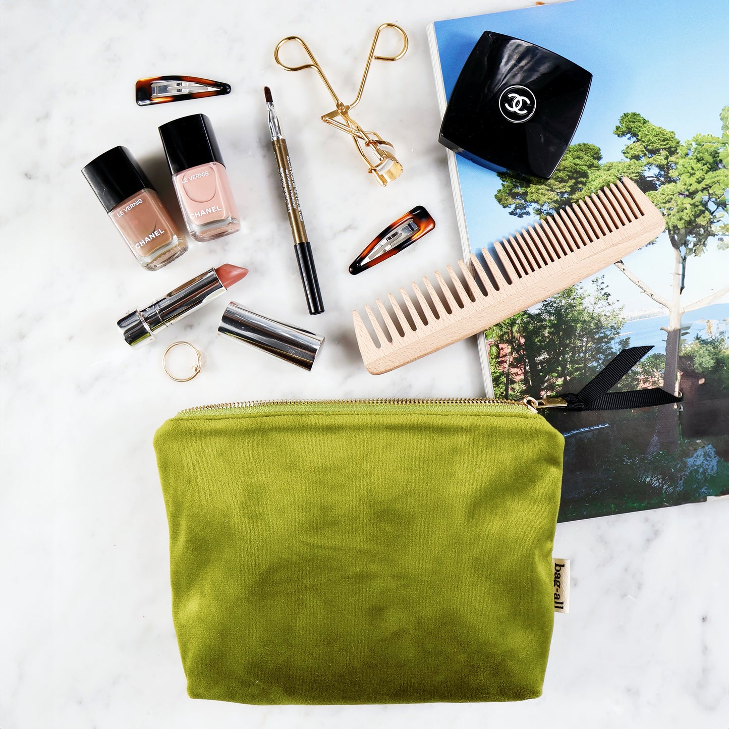 Bag-all My Makeup Pouch in luxurious green velvet with waterproof coated lining, displayed with beauty essentials including nail polish, eyelash curler, makeup brush, comb, and cosmetics on marble surface