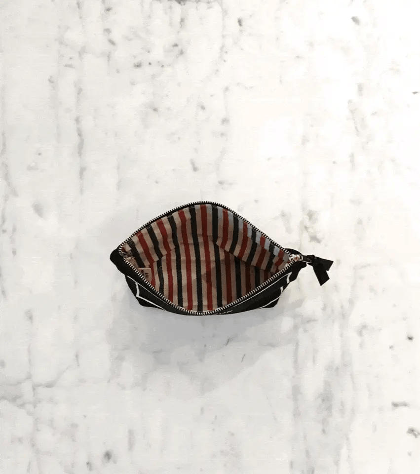Bag-all My Makeup Pouch in cream with waterproof striped interior lining, open to show spacious compartment for cosmetics and brushes, photographed on marble surface