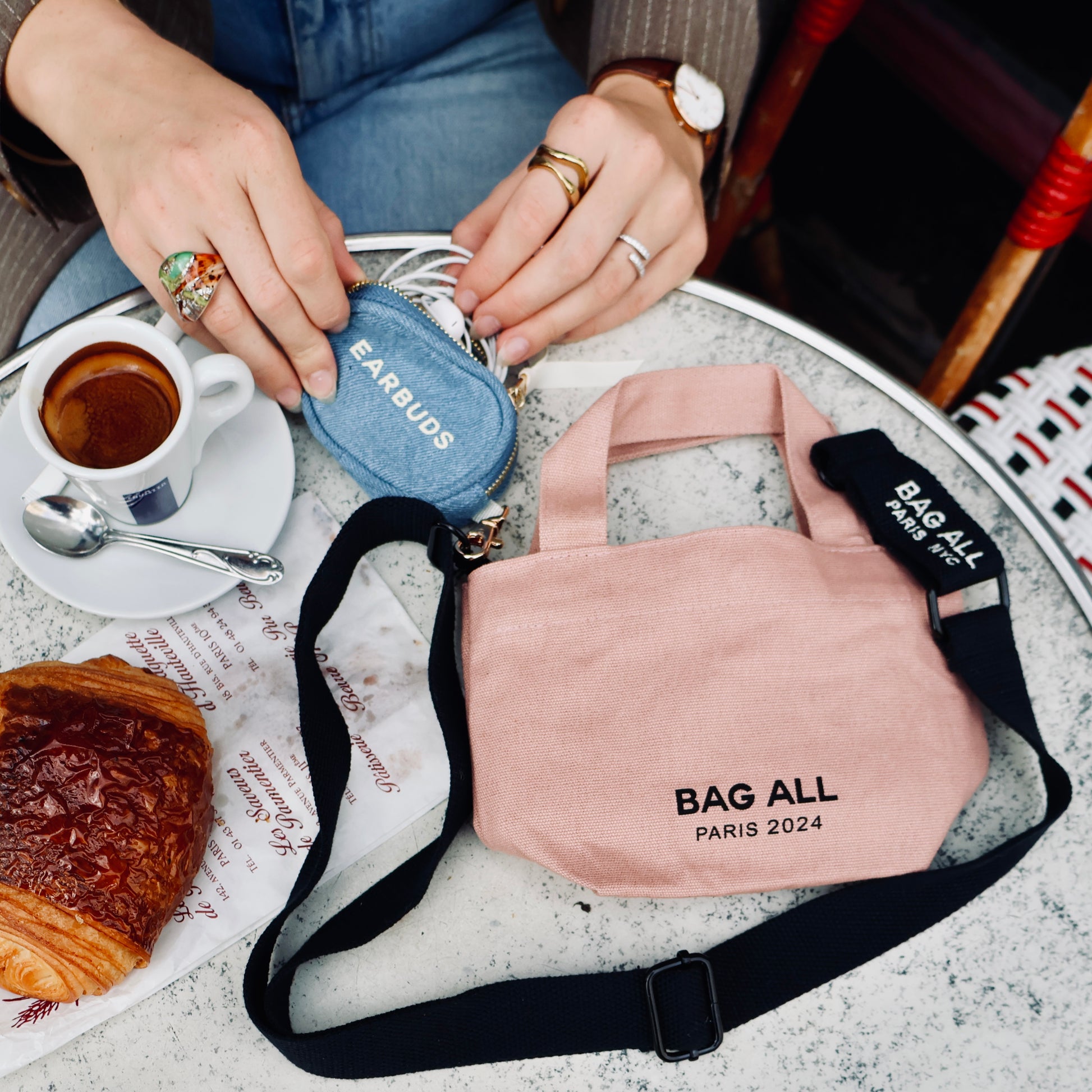 Bag-all Mini Tote Bag in blush pink with black strap displayed on marble cafe table with espresso and croissant, showcasing Paris 2024 branding and practical everyday style