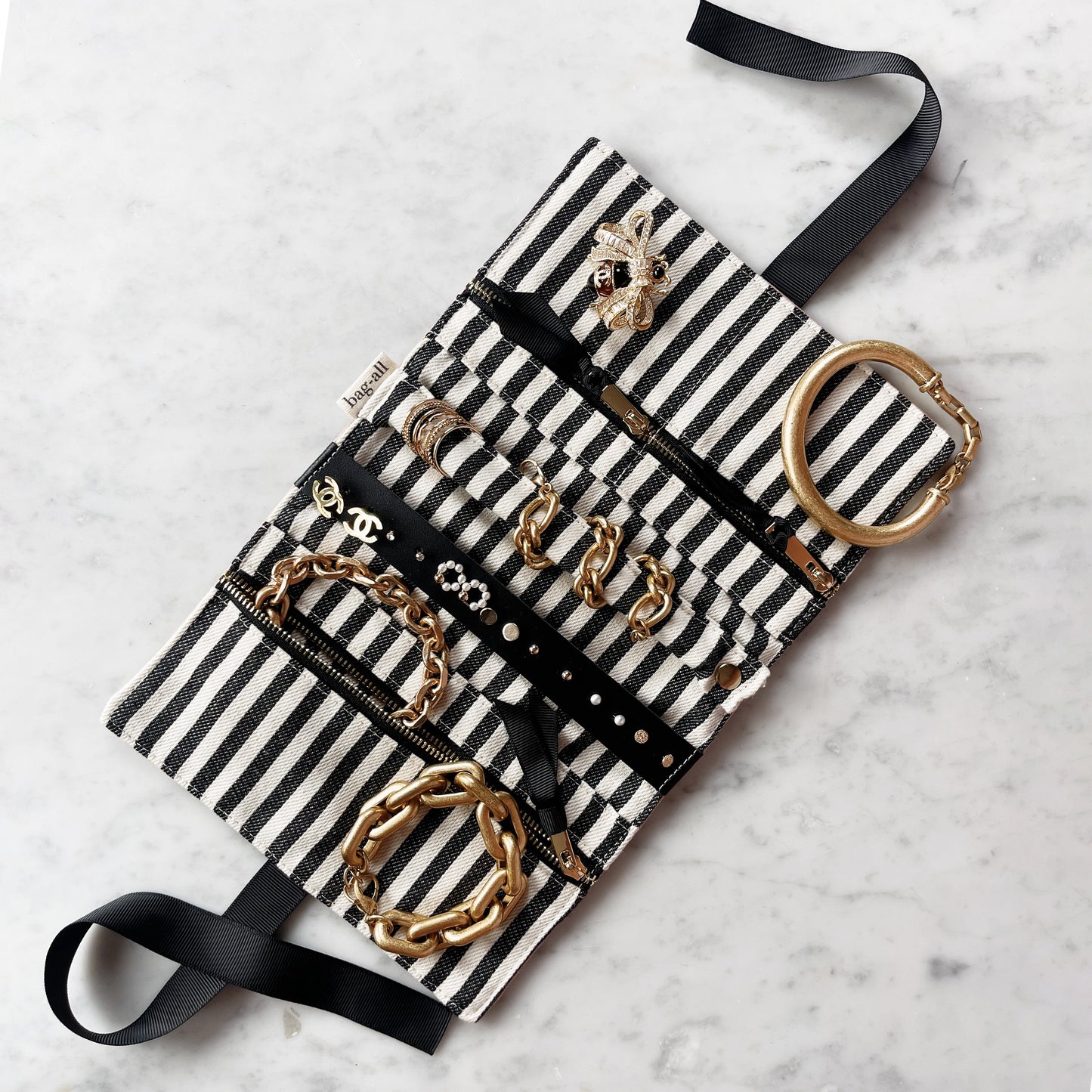 Bag-all Couture Jewelry Roll Medium in cream with black and white striped fabric, displaying organized jewelry storage with multiple compartments and gold accessories laid flat