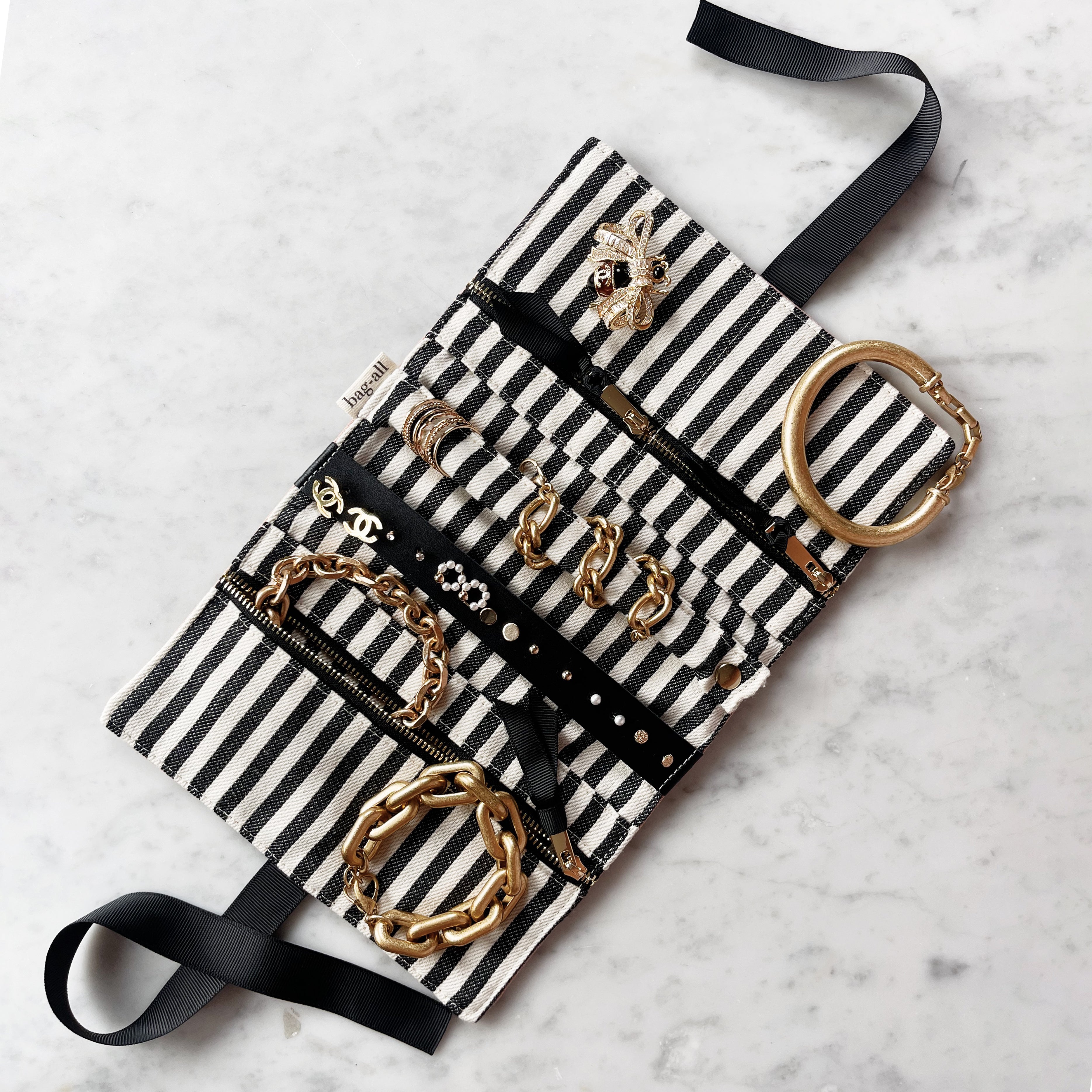 Bag-all Couture Jewelry Roll Medium in cream with black and white striped fabric, displaying organized jewelry storage with multiple compartments and gold accessories laid flat