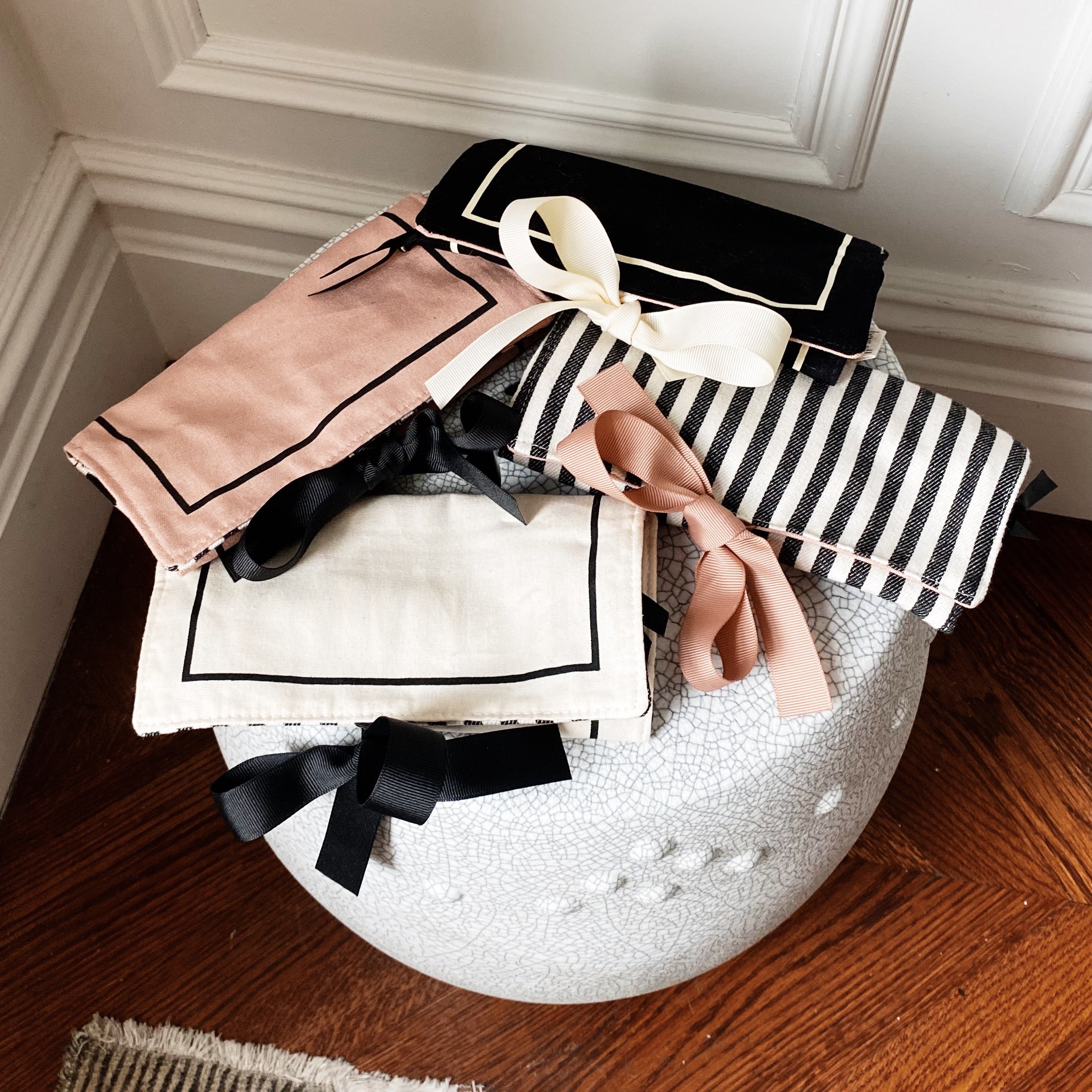Bag-all Couture Jewelry Roll Medium in pink with black and white striped lining, featuring three zipper compartments, leather earring holder, and padded ring section on white decorative surface