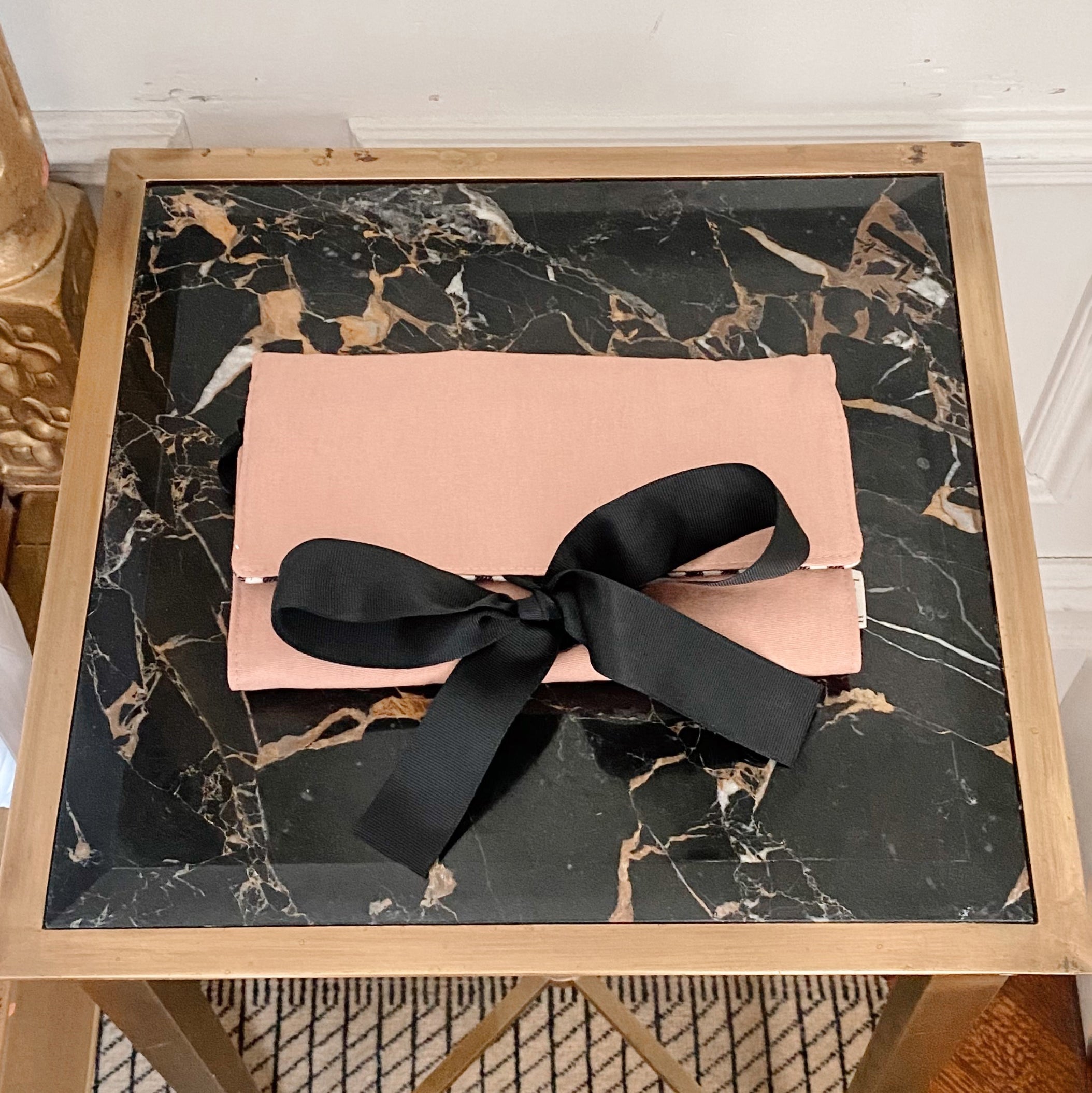 Bag-all Large Jewelry Roll in blush pink with black bow tie closure, displayed on marble surface. Elegant travel organizer for storing precious jewelry and accessories.