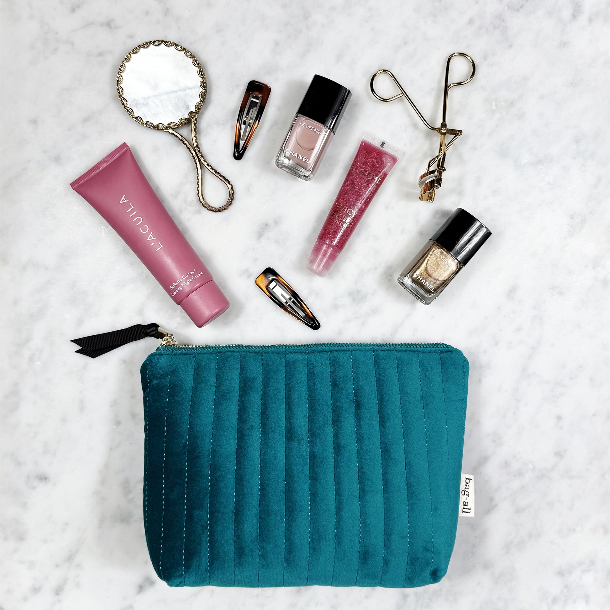 Bag-all teal quilted eco velvet makeup bag with cosmetics and beauty tools on marble surface