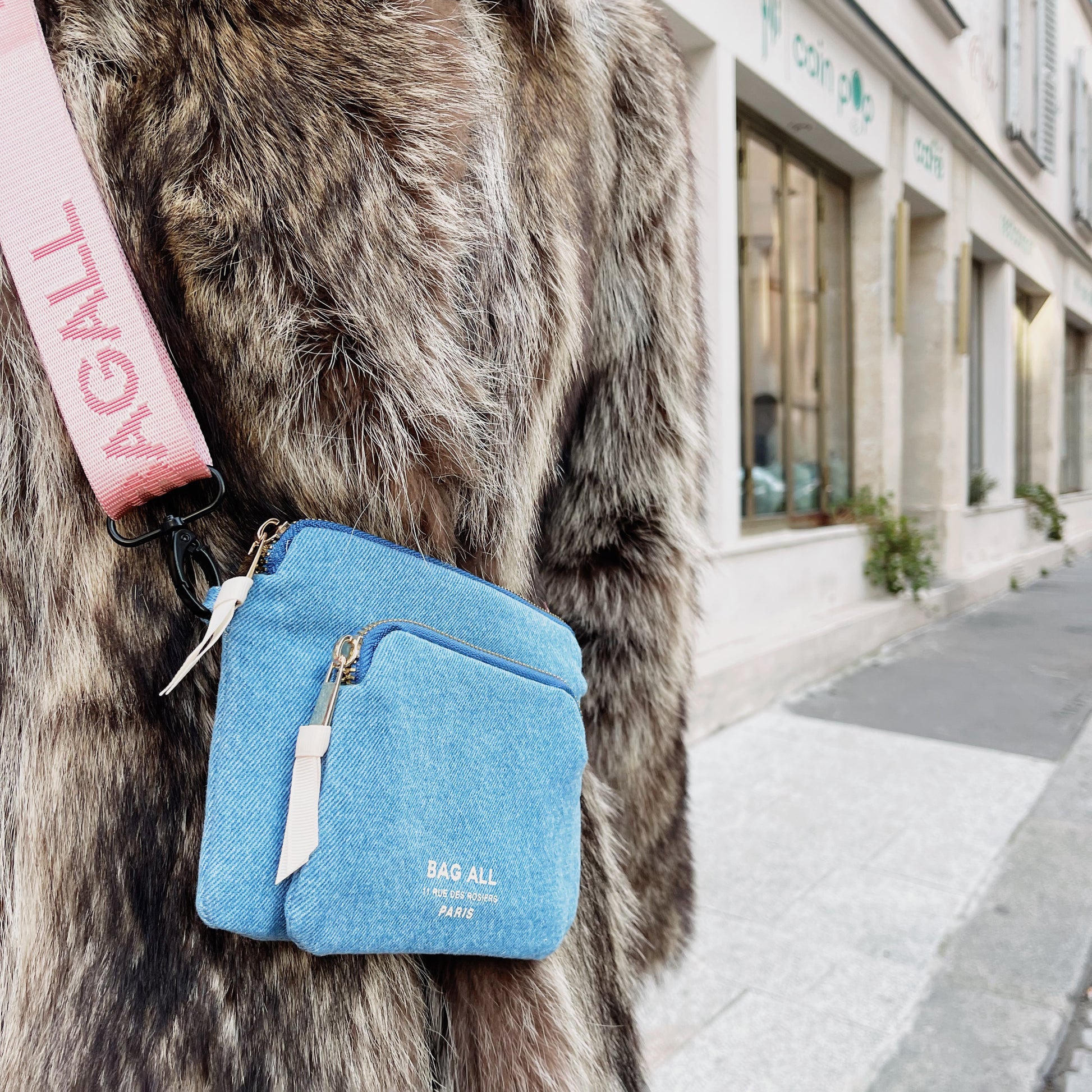 Bag-all Padded Trinket Pouch Double Pocket in denim blue, styled with pink strap against fur coat, showcasing compact design and versatile wear options in urban setting