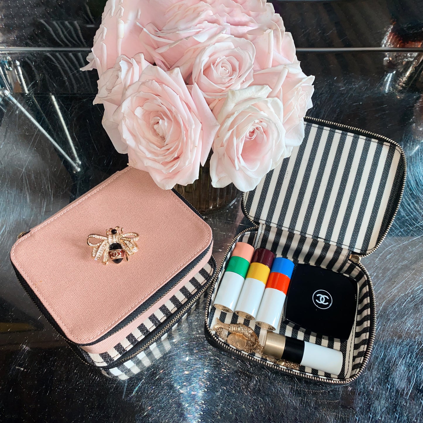 Bag-all pink Cosmetics/Trinket Box with gold bee embellishment, striped lining, and durable zipper, shown with makeup products and blush roses