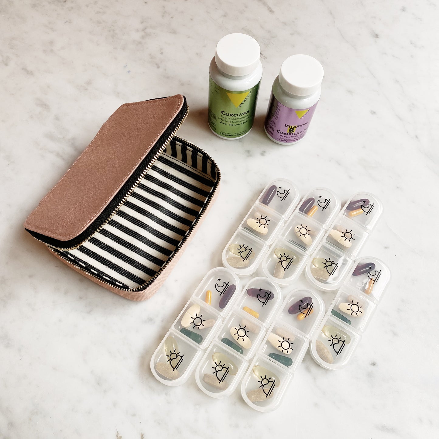 Bag-all Large Pill Travel Case in pink/blush with striped interior lining, featuring daily pill organizer compartments and vitamin bottles on marble surface, showcasing practical medication storage solution