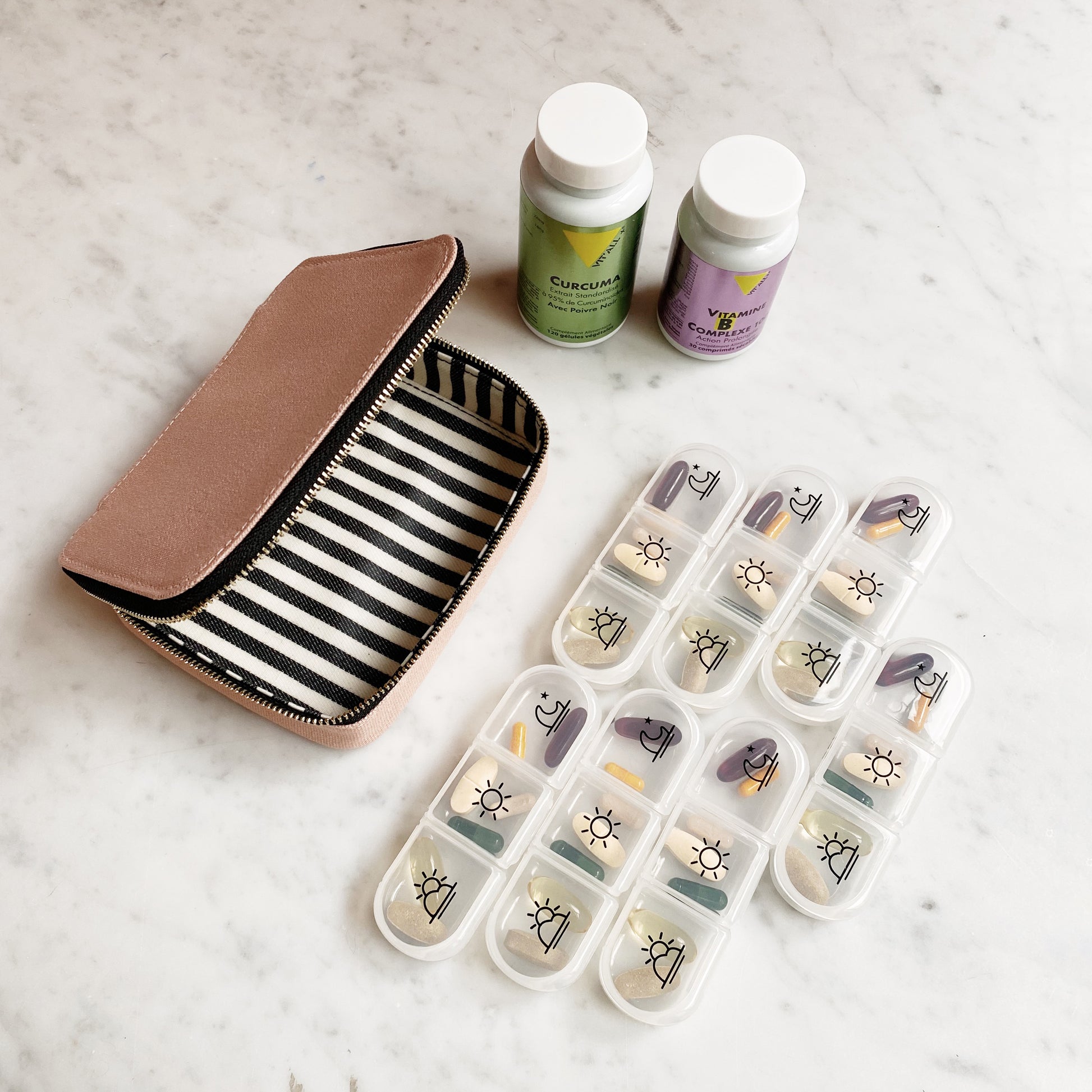 Bag-all Large Pill Travel Case in pink/blush with striped interior lining, featuring daily pill organizer compartments and vitamin bottles on marble surface, showcasing practical medication storage solution