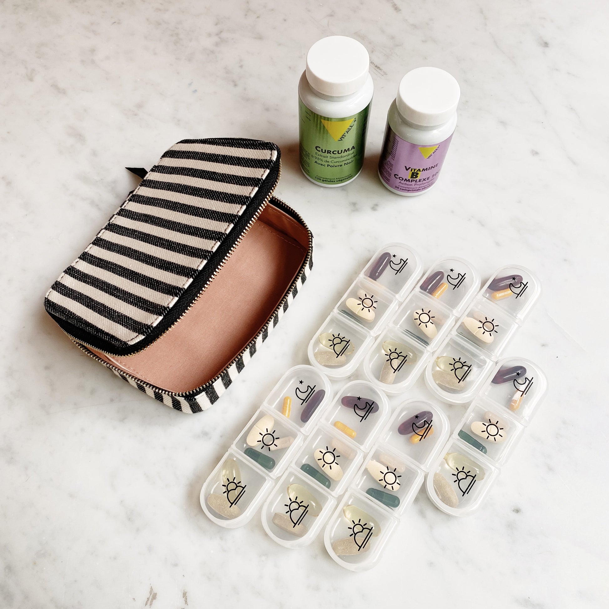 Bag-all Large Pill Travel Case with striped cotton exterior, daily organizer compartments, zipper closure, shown with medicine bottles and pill containers on marble surface.