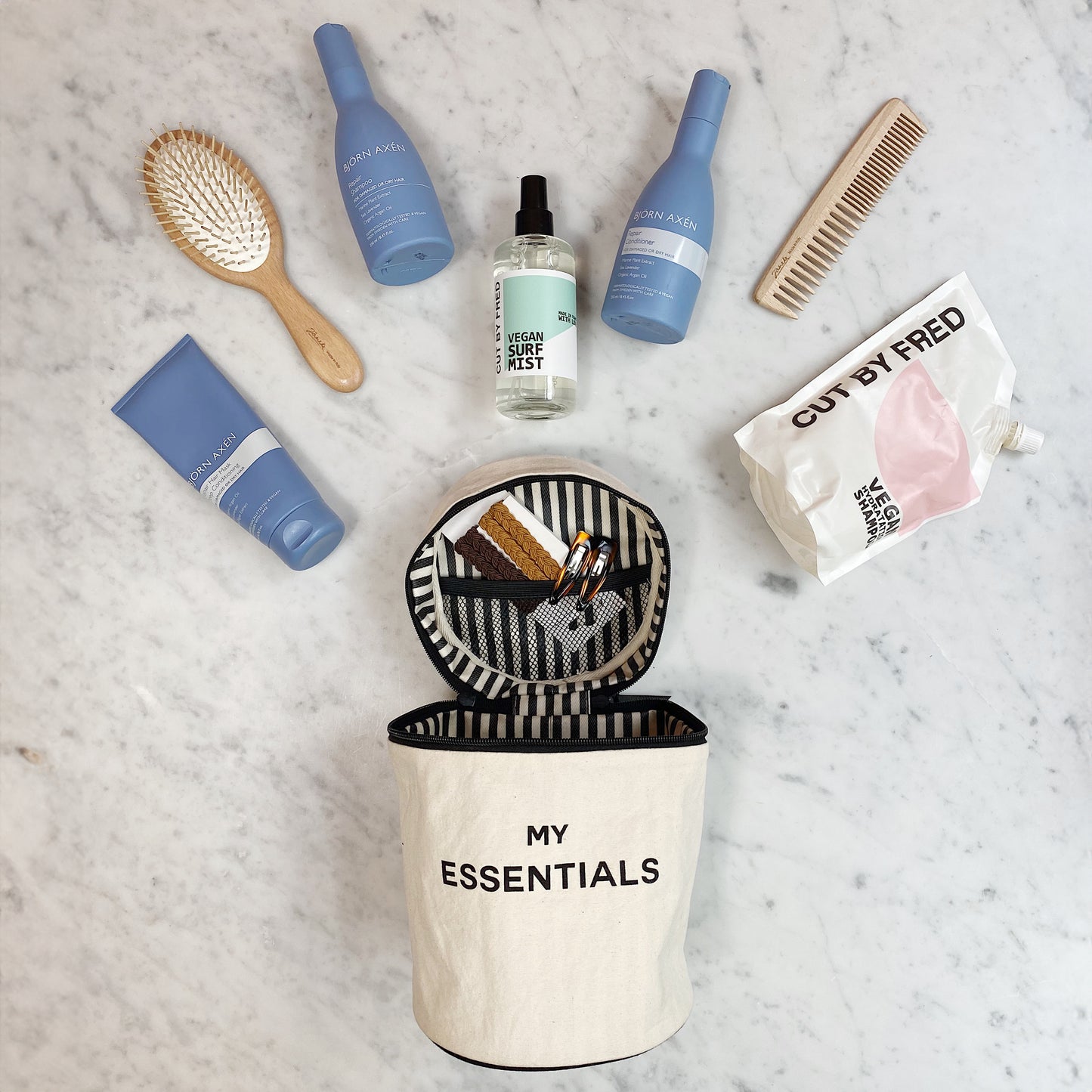 Bag-all Roomy Travel Essentials Case in cream with striped interior, shown open displaying haircare products, brush, and beauty items on marble surface, demonstrating spacious storage capacity and organization features