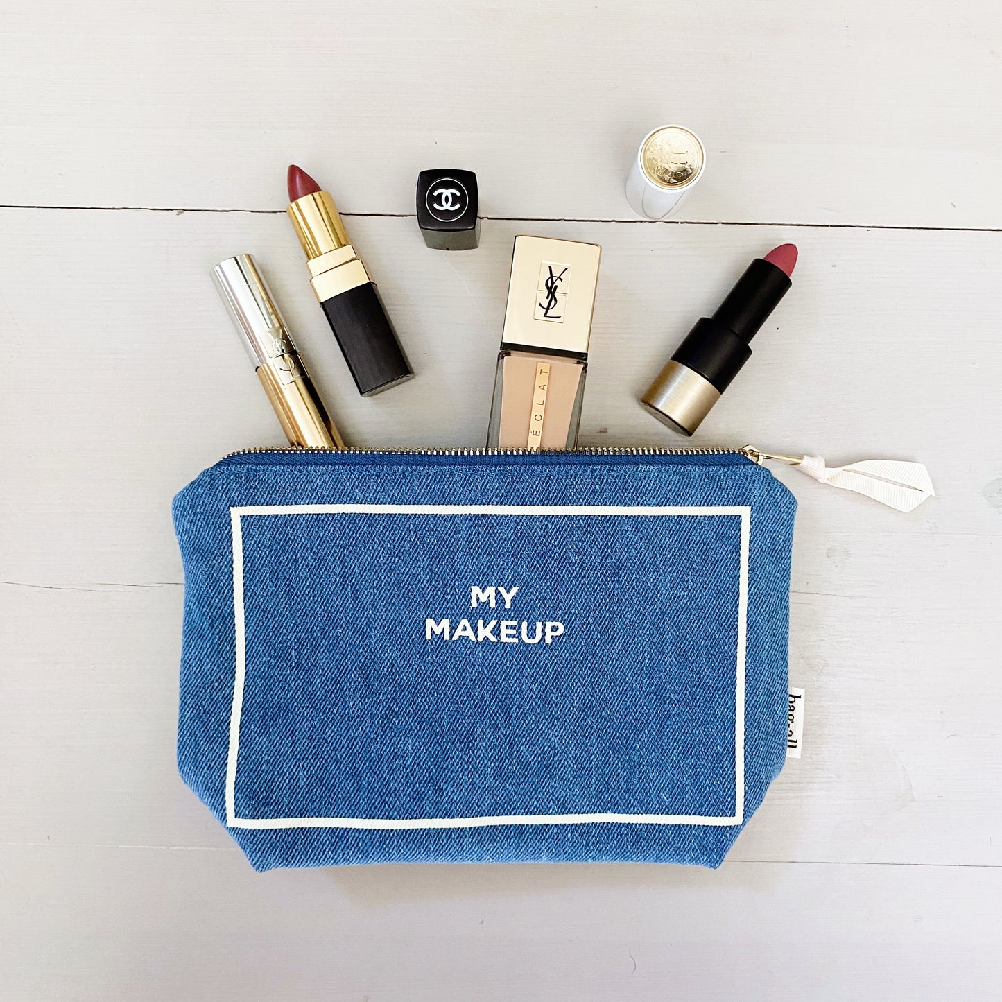 Bag-all My Makeup Pouch in denim with waterproof lining, shown with luxury cosmetics, featuring white text embroidery and zipper closure, perfect for organizing beauty essentials