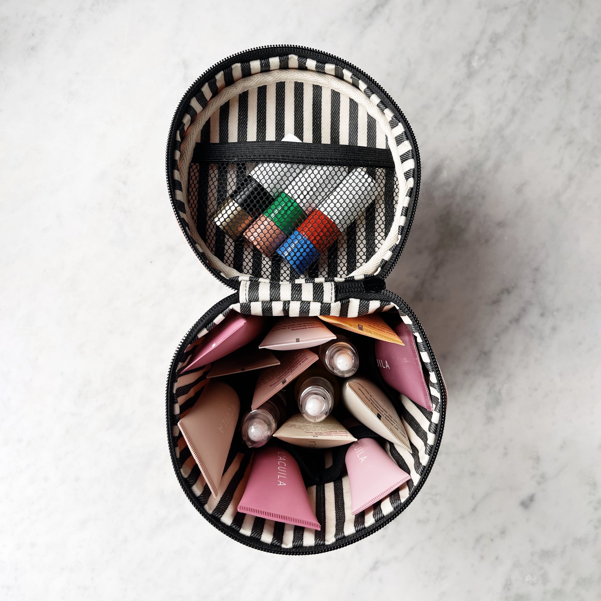 Bag-all Round My Skin Care Case in Pink/Blush featuring striped interior, mesh pocket, and organized compartments for beauty products on marble surface