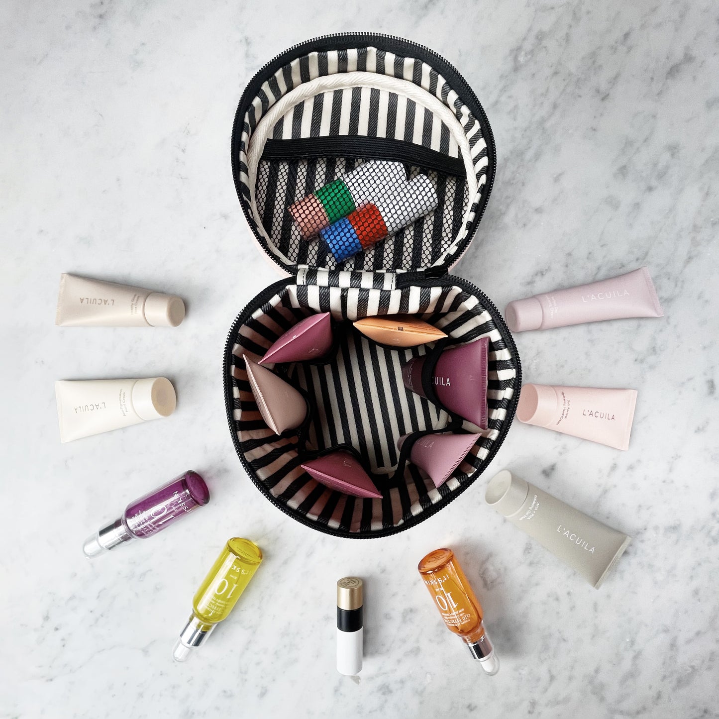 Bag-all Round My Skin Care Case in cream with striped interior, showcasing organized compartments and mesh pocket, displayed with skincare products on marble surface