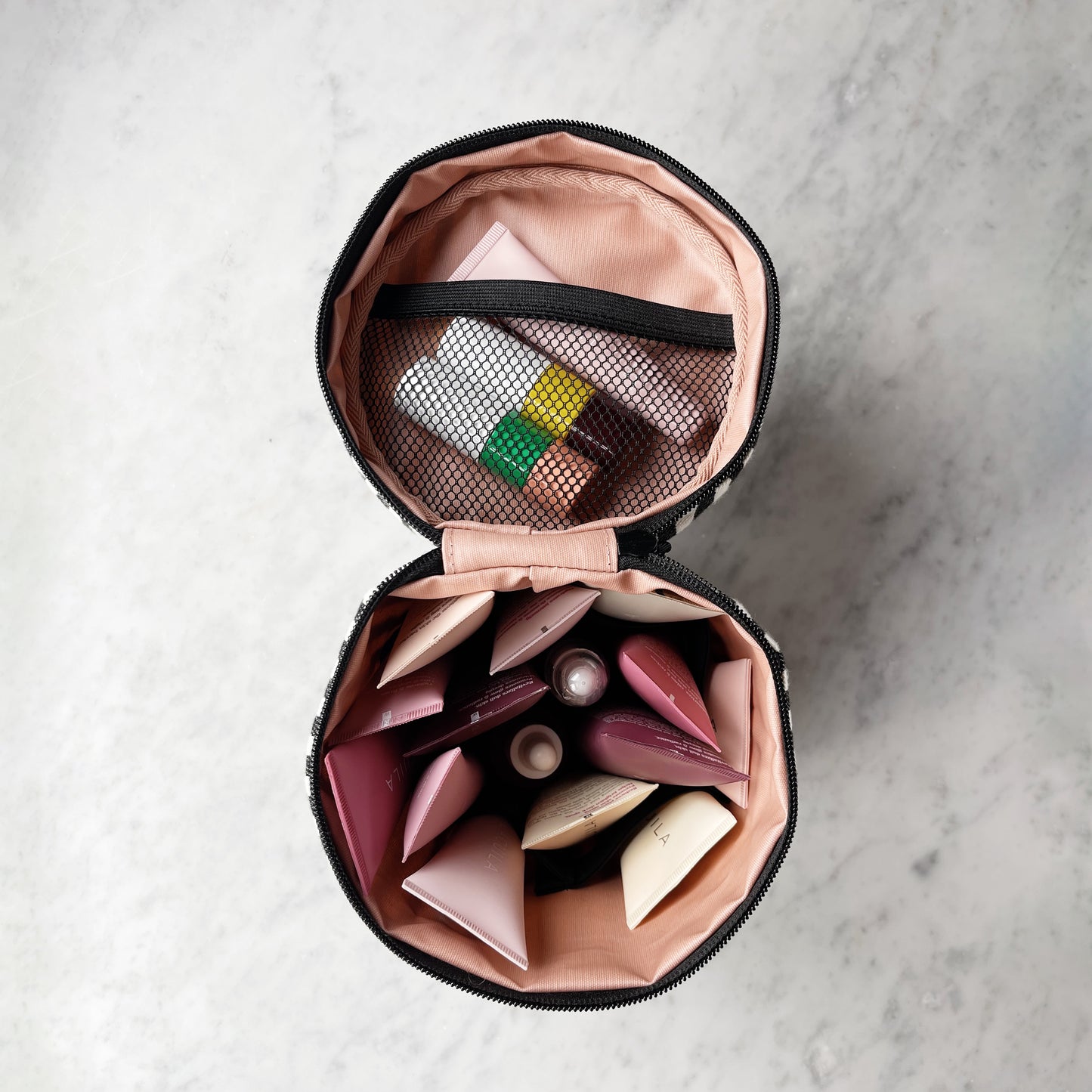 Bag-all Round My Skin Care Case in striped pattern, opened to show pink interior compartments and mesh pocket, displaying organized skincare storage solution on marble surface