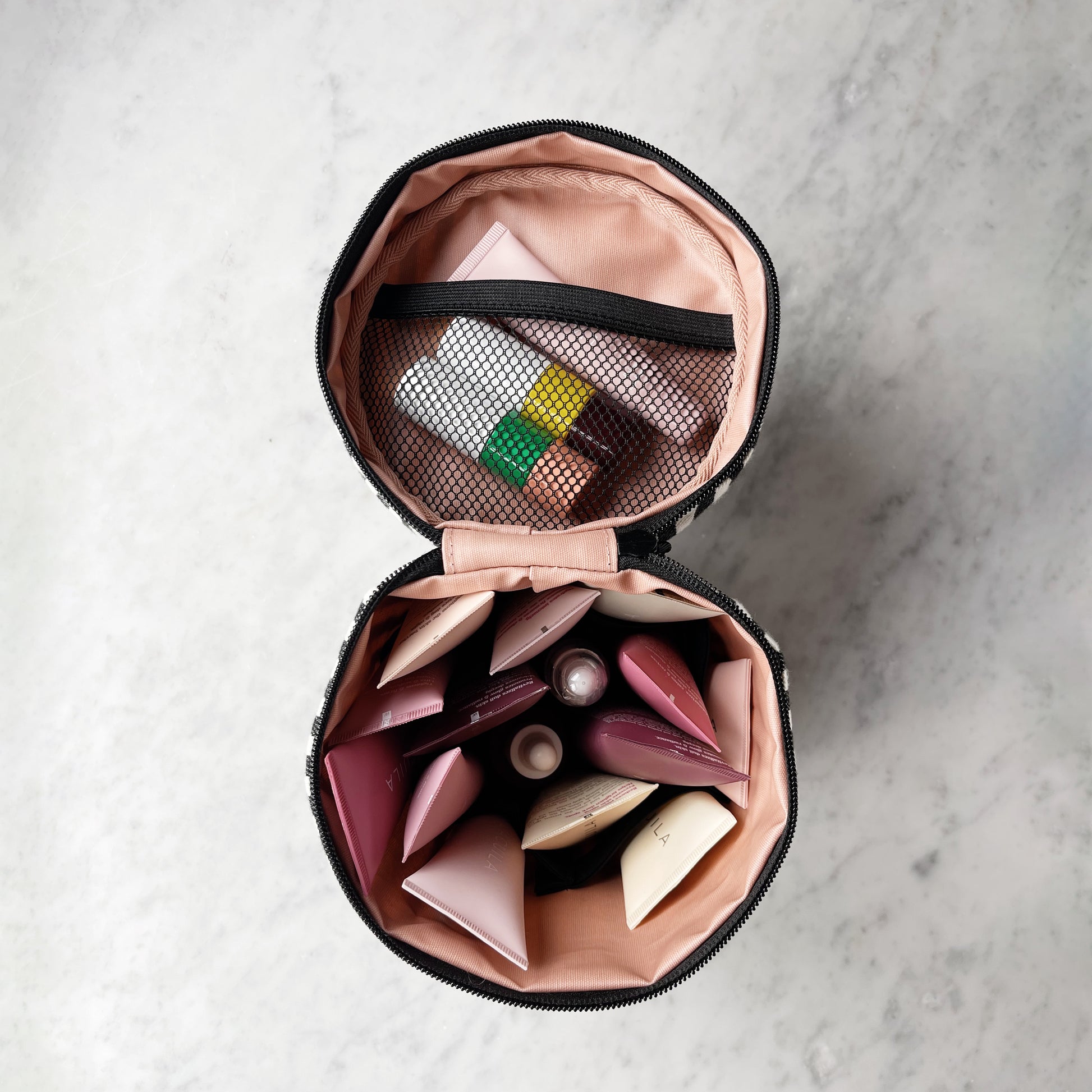 Bag-all Round My Skin Care Case in striped pattern, opened to show pink interior compartments and mesh pocket, displaying organized skincare storage solution on marble surface