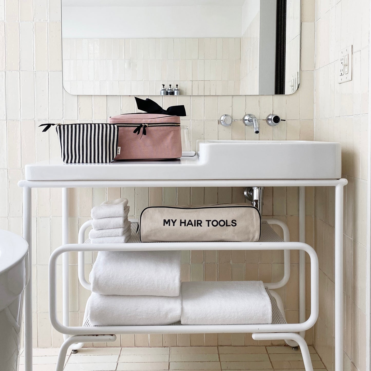 Bag-all Striped Makeup Pouch with pink coated lining displayed on white bathroom vanity shelf alongside hair tools organizer and folded towels, showcasing modern bathroom organization and storage