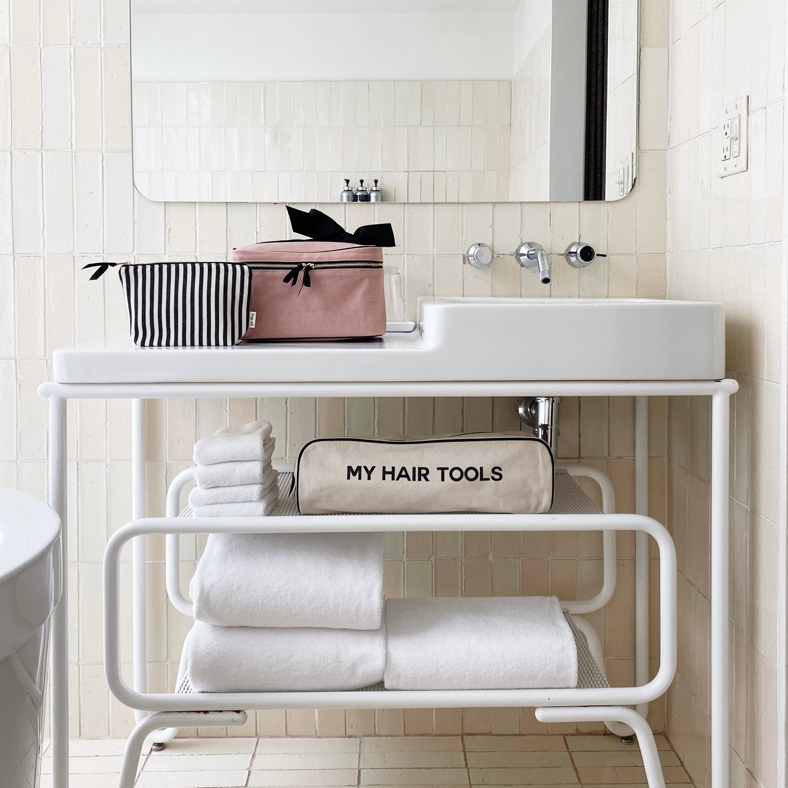 Bag-all Striped Makeup Pouch with pink coated lining displayed on white bathroom vanity shelf alongside hair tools organizer and folded towels, showcasing modern bathroom organization and storage