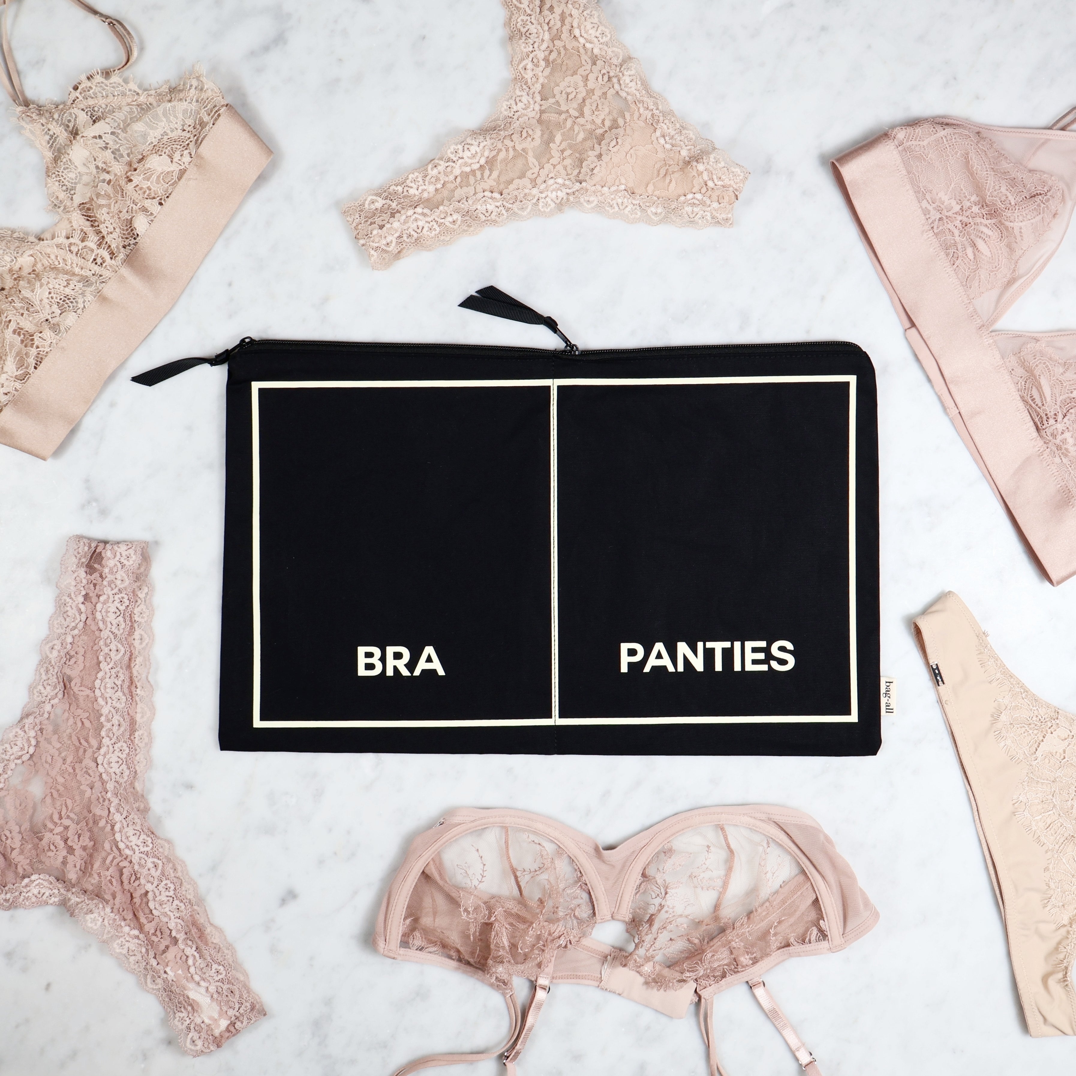 Black Bag-all lingerie organizer pouch labeled bra and panties surrounded by lace lingerie on marble surface