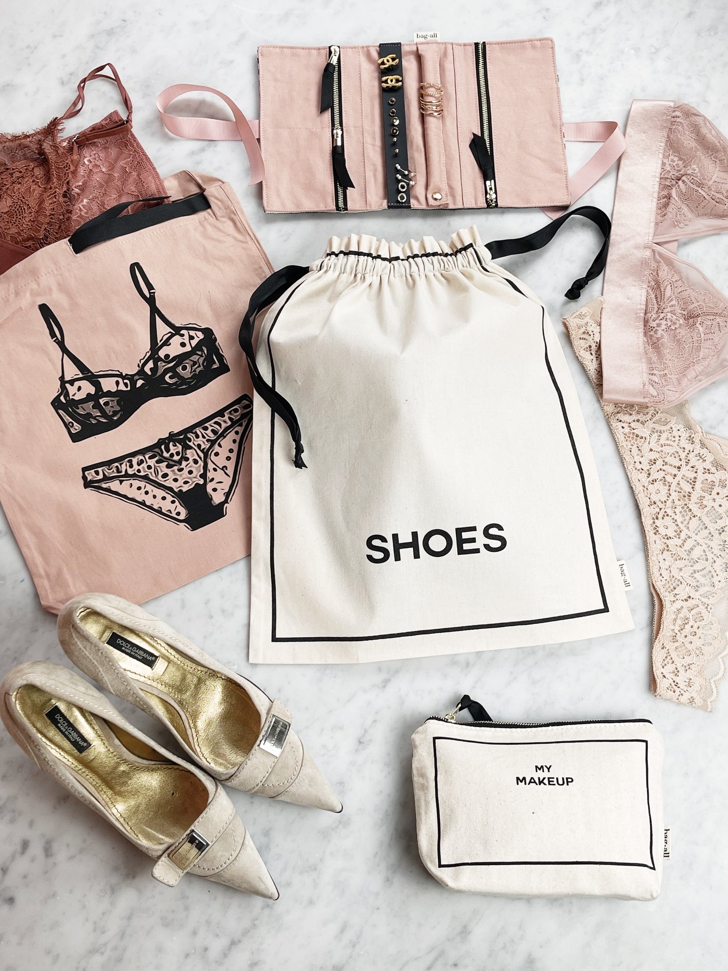 Bag-all Couture Shoe Travel Bag in cream cotton with black text, shown with luxury shoes and travel accessories on marble surface, perfect for organized travel and storage