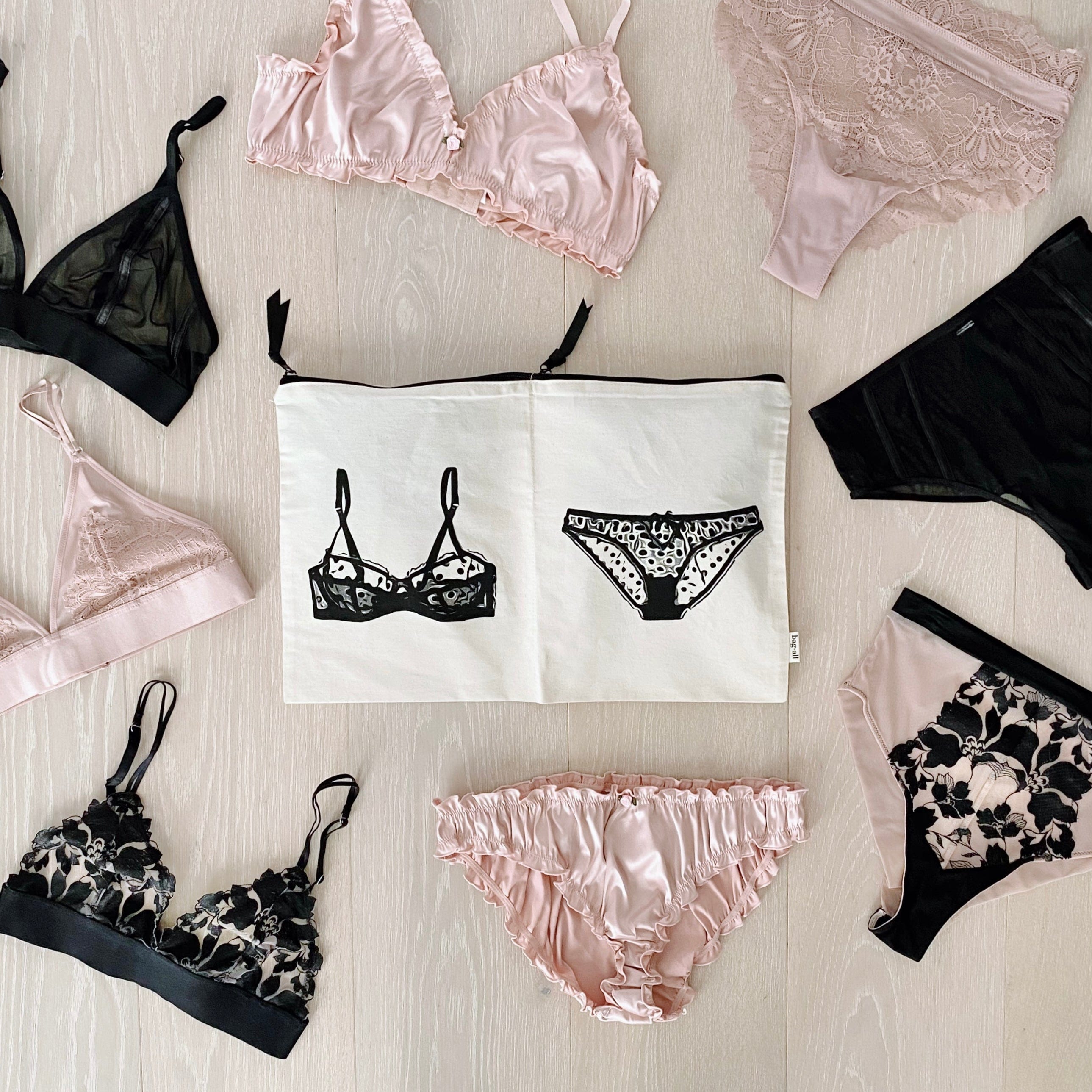 Bag-all Travel Glam 4-Pack organizer set with lingerie pouches displayed with pink and black lace bralettes and matching underwear, showcasing elegant storage solutions for intimate apparel