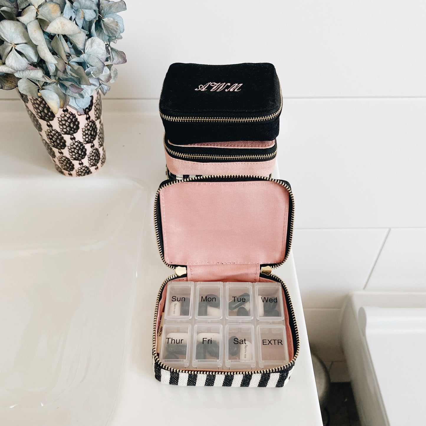 Bag-all Striped Pill Organizing Case featuring a weekly pill organizer, monogram option, and dual-compartment design with black and white stripes and pink interior. Compact travel medication storage.