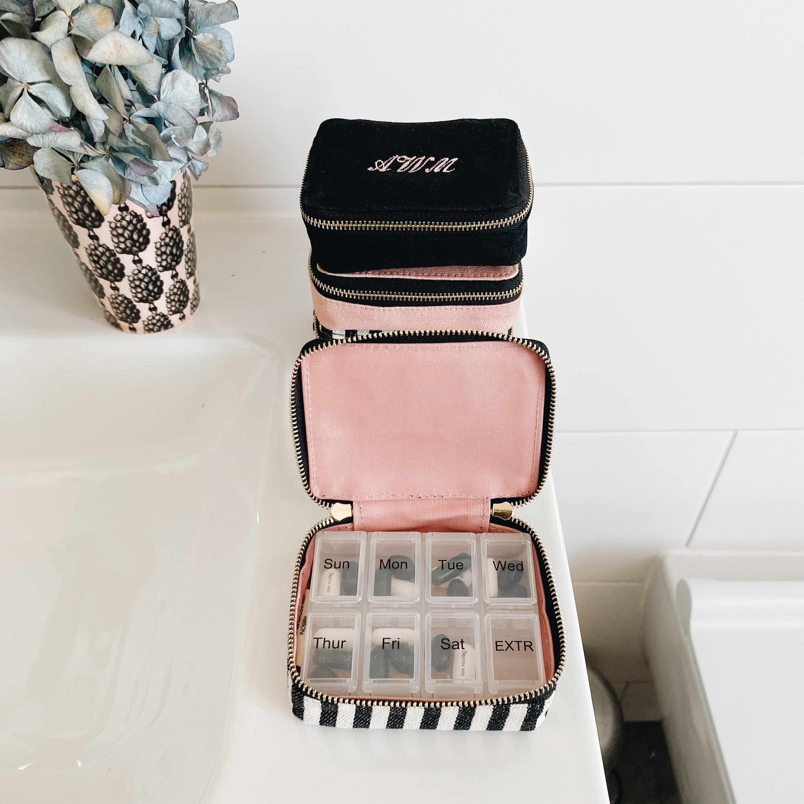 Bag-all Striped Pill Organizing Case featuring a weekly pill organizer, monogram option, and dual-compartment design with black and white stripes and pink interior. Compact travel medication storage.