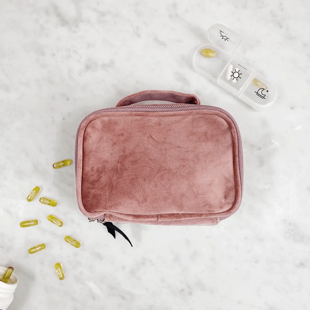 Bag-all Pink Velvet Pill Box with Handle & Weekly Organizer shown with supplement capsules and daily pill container on marble surface, showcasing portable medication storage solution