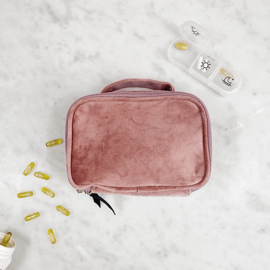 Bag-all Pink Velvet Pill Box with Handle & Weekly Organizer shown with supplement capsules and daily pill container on marble surface, showcasing portable medication storage solution
