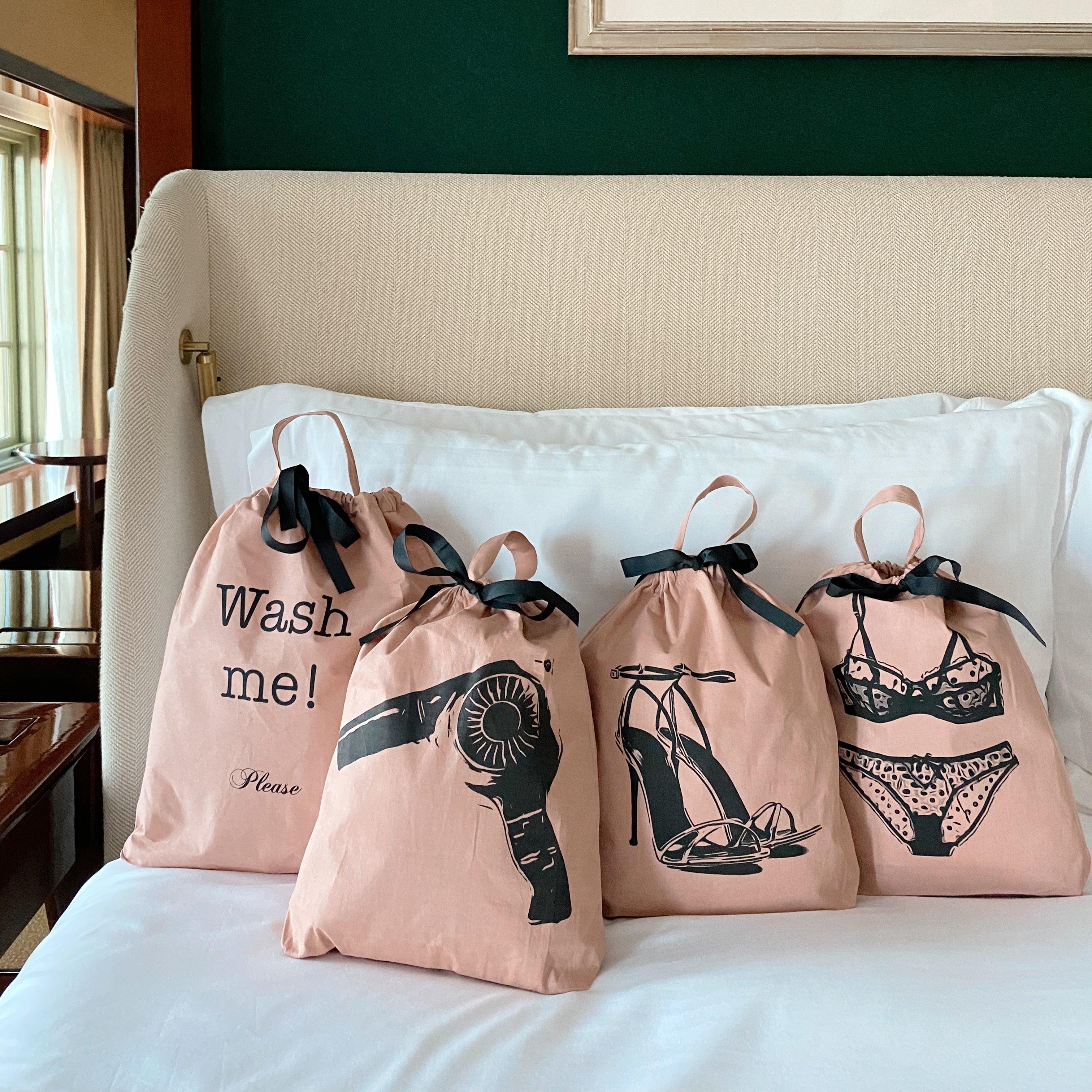 Bag-all pink cotton travel organizer bags featuring fun laundry graphics, including Hair Dryer Travel Bag with printed hairdryer design, black ribbons, and drawstring closure on cream sofa setting