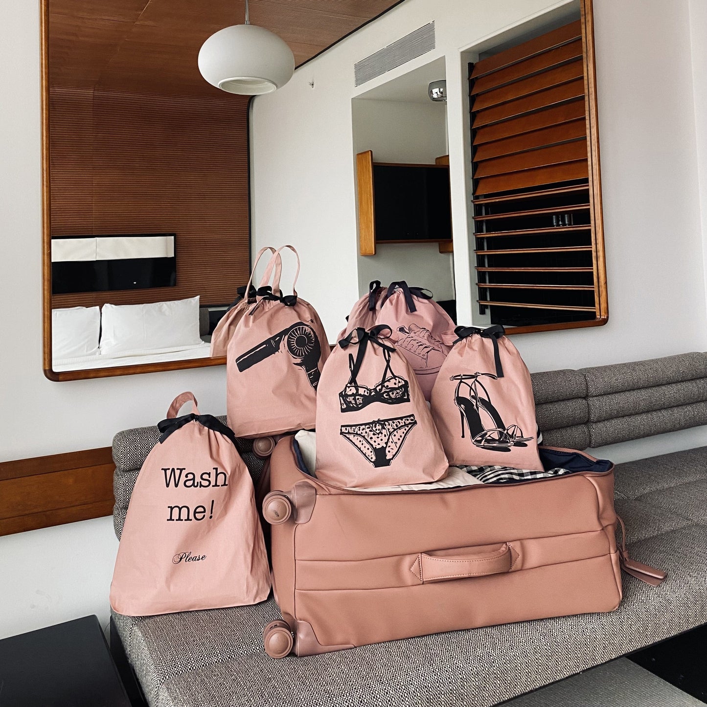 Bag-all Tennis Sneaker Shoe Bag in pink cotton with gray print design, shown alongside matching travel organizer bags featuring lingerie and wash illustrations, displayed on gray couch