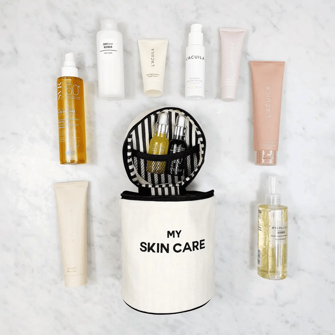 Bag-all Round Skin Care Case with Handle in cream color, surrounded by various skincare products on marble surface, featuring striped interior and organized compartments