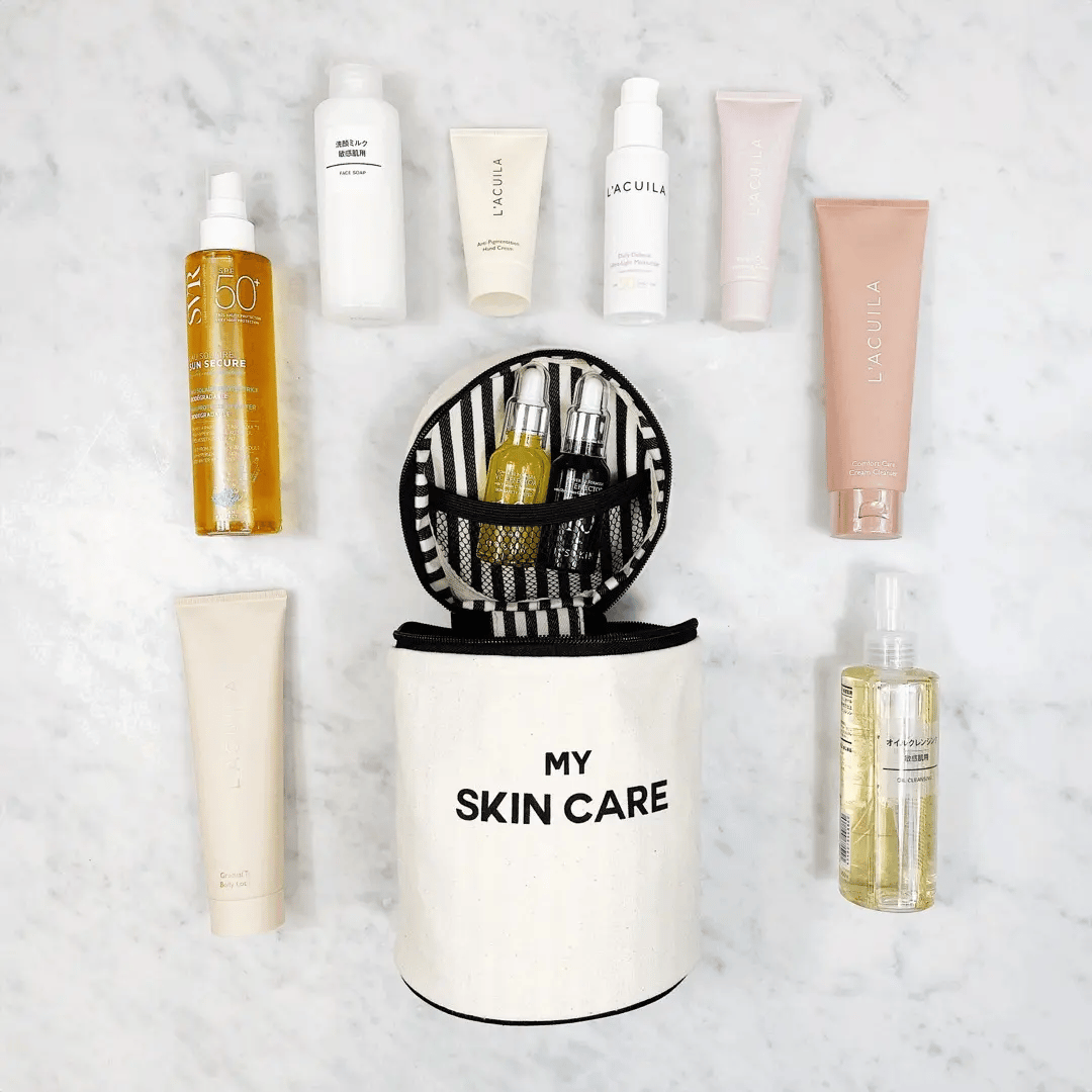 Bag-all Round Skin Care Case with Handle in cream color, surrounded by various skincare products on marble surface, featuring striped interior and organized compartments