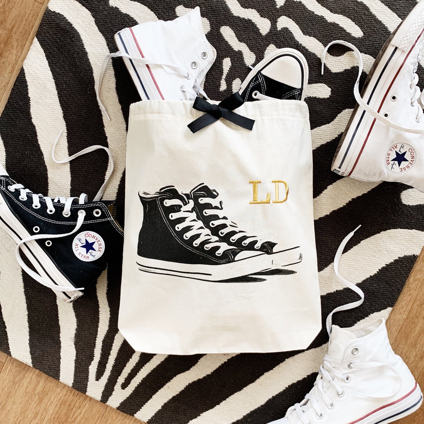 Bag-all Cream Sneakers Shoe Bag with black high-top sneaker design and gold monogram LD, displayed on zebra print background with white converse shoes